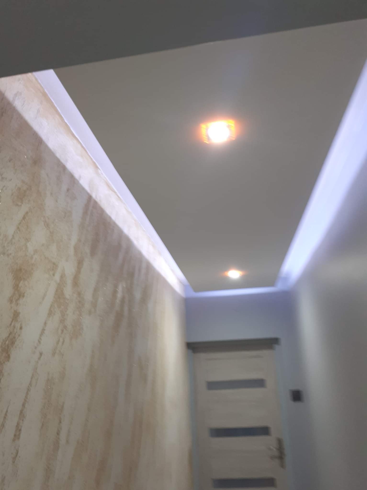 Wykończony korytarz z dekoracyjną ścianą, podwieszanym sufitem z oświetleniem punktowym i ledowym. Widoczna biała stolarka drzwiowa.