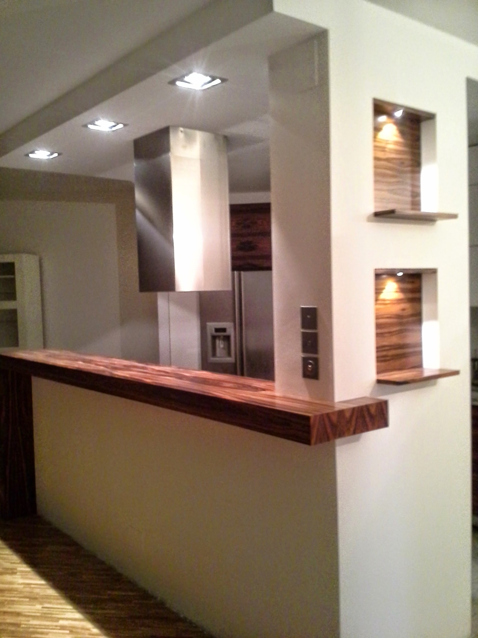 Nowoczesna kuchnia z drewnianym blatem i wnękami oświetleniowymi. Wykończenie wnętrz w Katowicach. Widoczny fragment podłogi i okap.