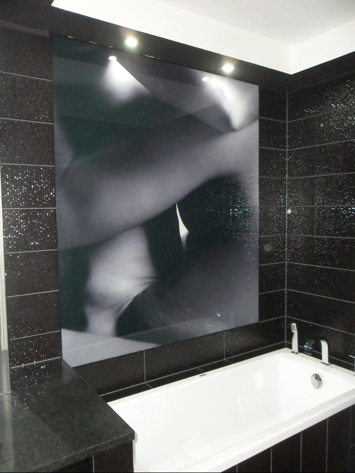 Nowoczesna łazienka z czarnymi płytkami i dużą grafiką na ścianie. Biała wanna z chromowaną armaturą. Oświetlenie punktowe podkreśla detale.