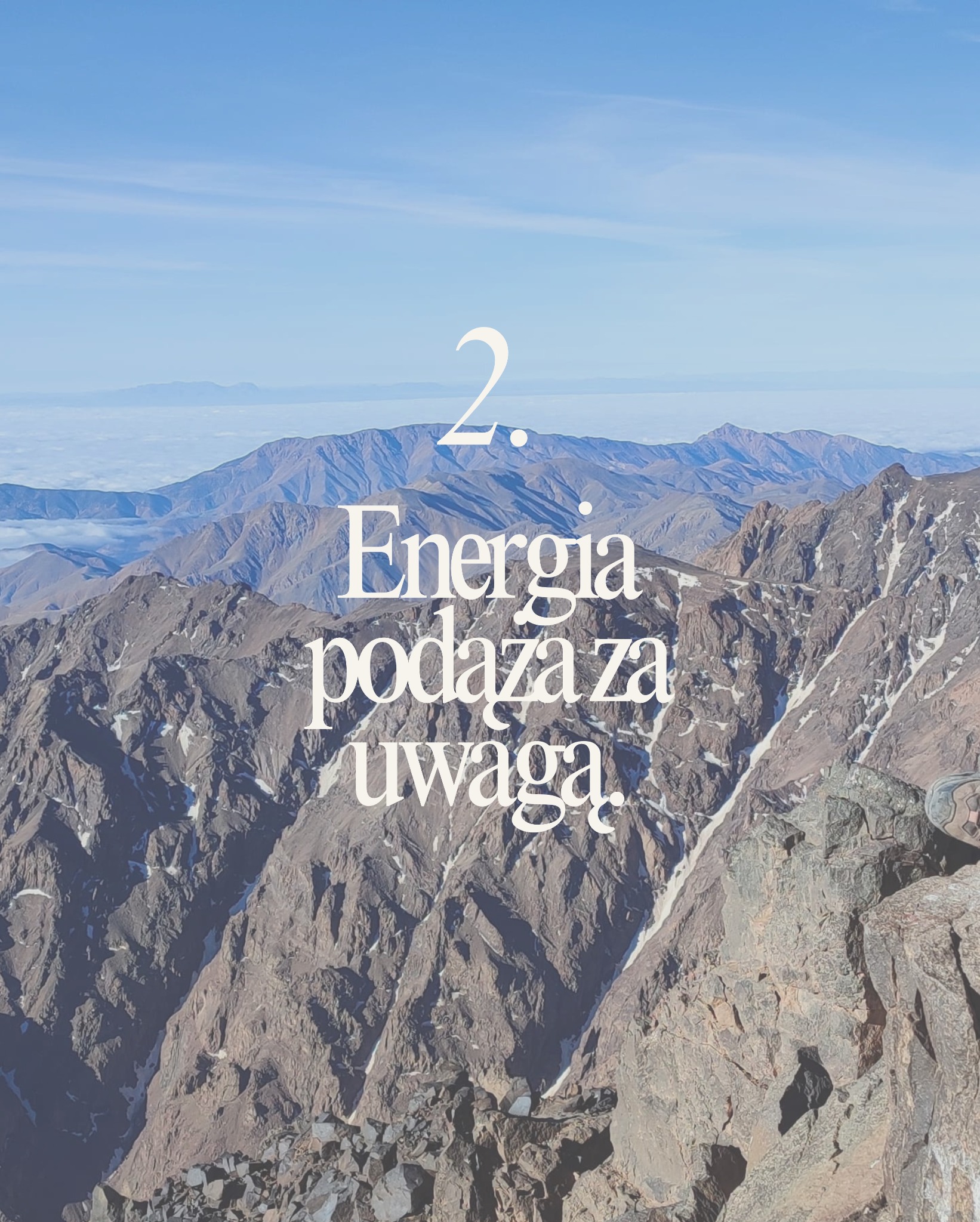 Górzysty krajobraz z widoczną perspektywą z wysokości, błękitne niebo i chmury w tle. Na pierwszym planie tekst 'Energia podąża za uwagą'.