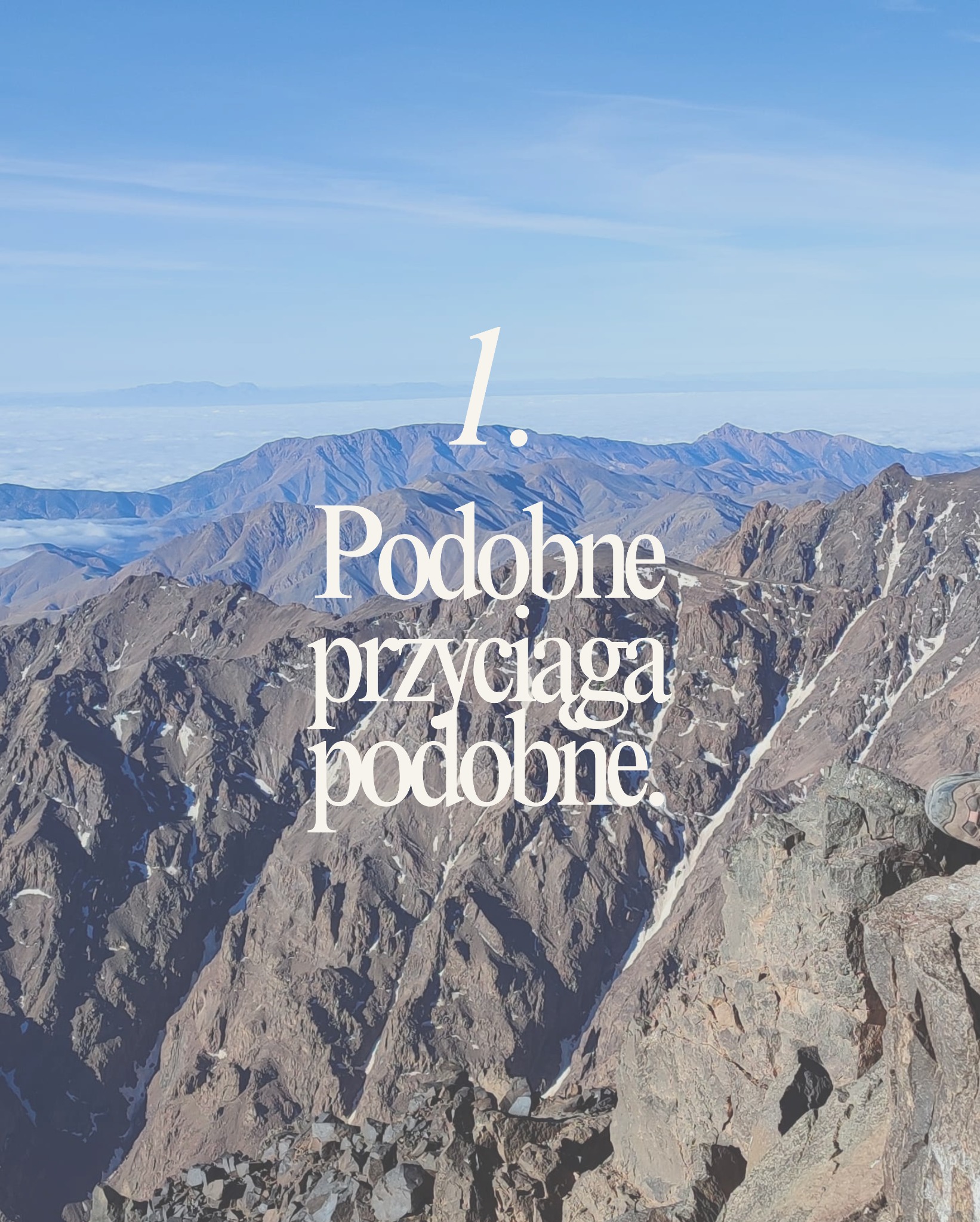 Górzysty krajobraz z napisem 'Podobne przyciąga podobne' w jasnej tonacji, błękitne niebo w tle. Ujęcie z góry, widoczny fragment buta w prawym dolnym rogu.