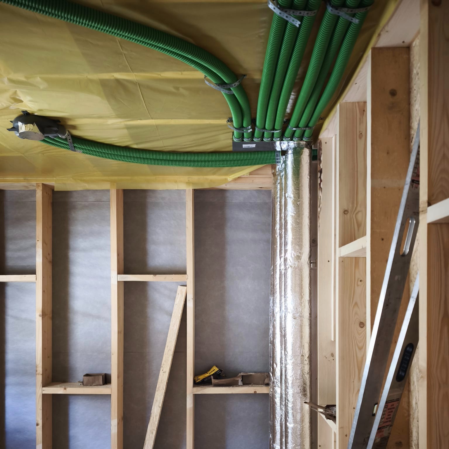 Zielone, karbowane rury wentylacyjne przymocowane do sufitu w surowym wnętrzu. Widoczna aluminiowa rura i drewniana konstrukcja szkieletowa ściany.