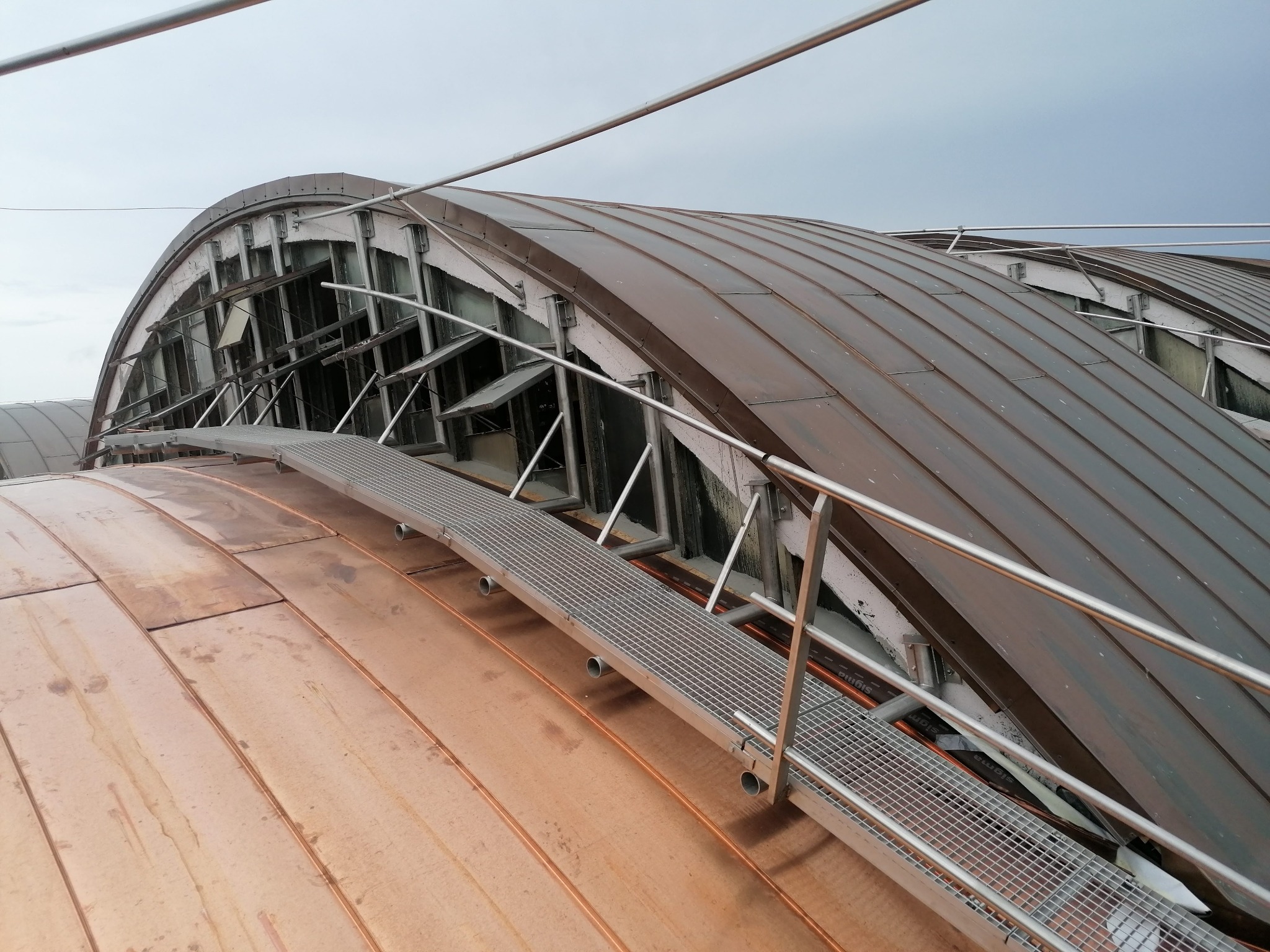 Metalowa konstrukcja dachu z elementami balustrady i pomostu roboczego, widok z góry, ukazujący detale łączeń i materiałów.