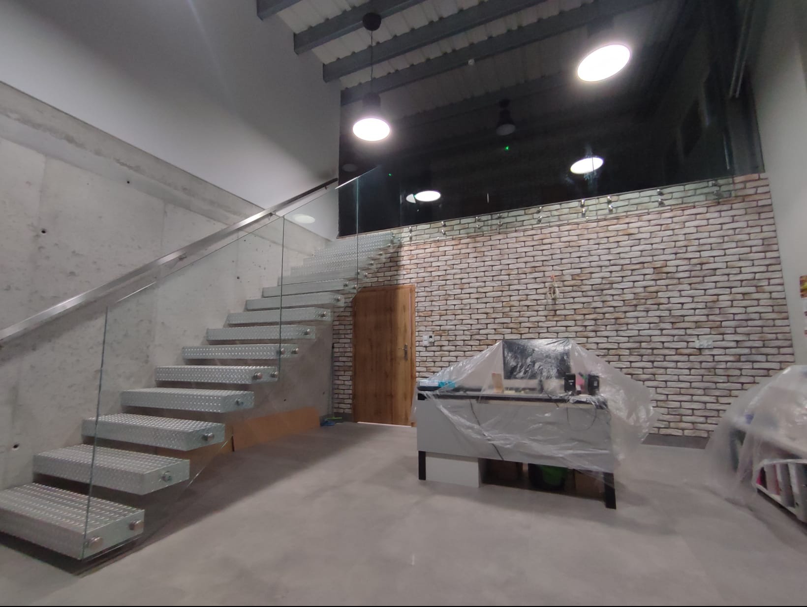 Metalowe schody z balustradą szklaną w nowoczesnym wnętrzu w Nowym Mieście Lubawskim. Stopnie z blachy ryflowanej, mocowania szkła punktowe.