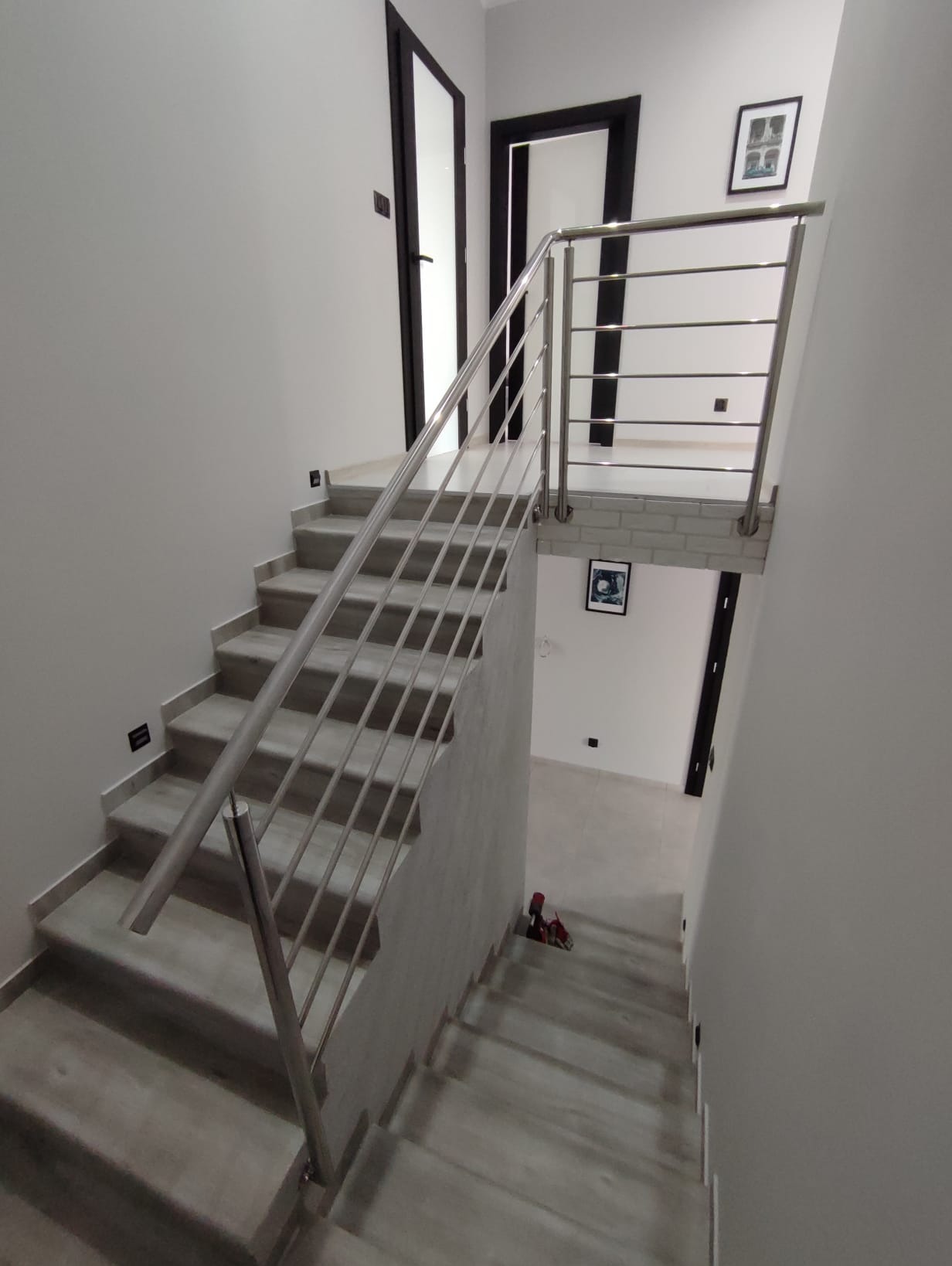 Nowoczesne schody z metalową balustradą w jasnym wnętrzu. Minimalistyczny design, szare stopnie, stalowe poręcze, czarne ramy drzwi. Widok z góry.