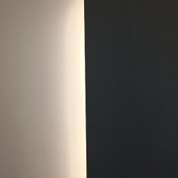 usługi budowlane - Fragment ściany po malowaniu na dwa kolory: jasny beż i grafit. Widoczne ostre przejście między kolorami i delikatne oświetlenie.