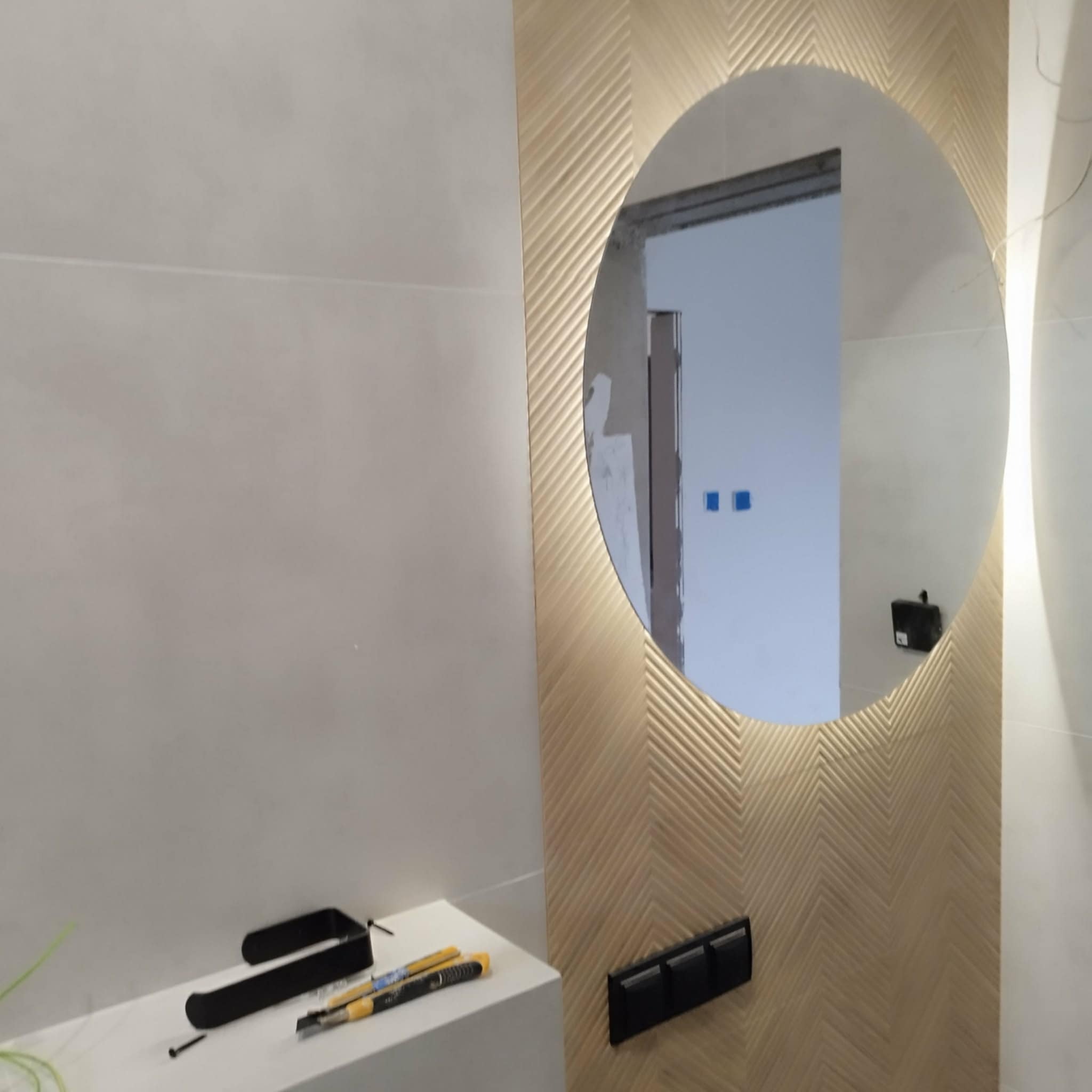 Wykończona łazienka z okrągłym lustrem z podświetleniem LED i dekoracyjną ścianą w jodełkę. Na blacie widoczne narzędzia i akcesoria łazienkowe.