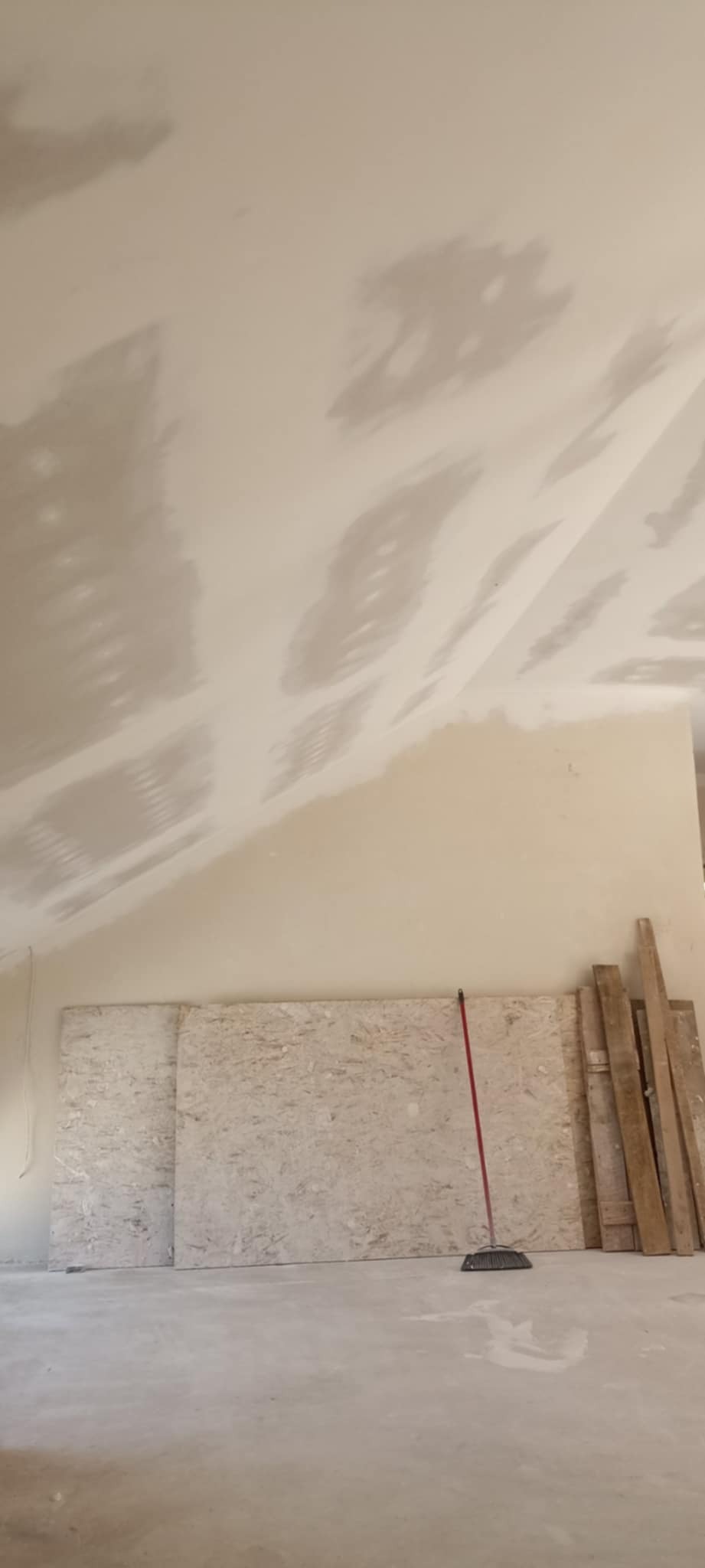 Sufit po szpachlowaniu, widoczne łączenia płyt gipsowych. Na podłodze płyty OSB, deski i miotła. Przygotowanie do dalszych prac wykończeniowych.