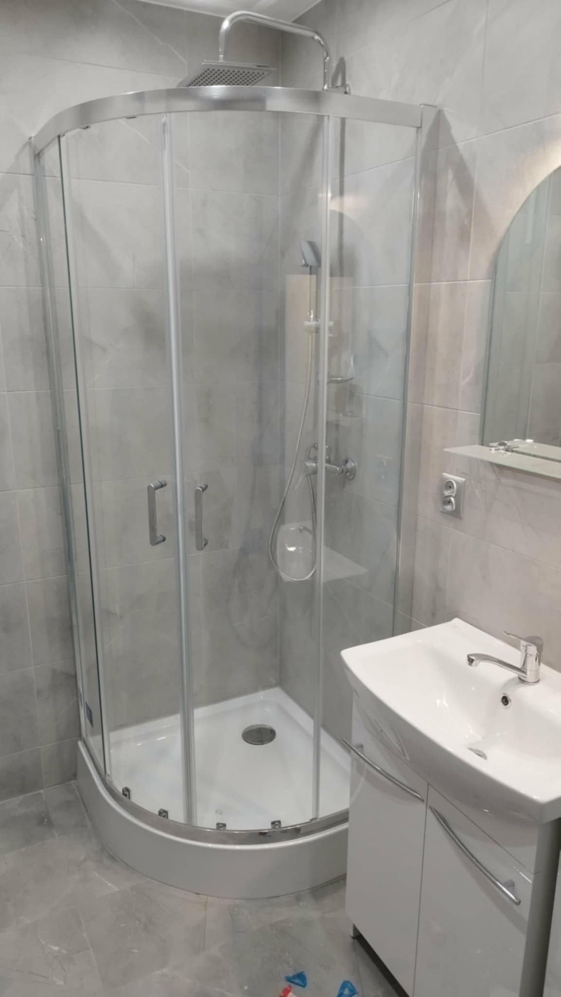 Nowoczesna kabina prysznicowa z hydromasażem i umywalką w odcieniach szarości, wykończona płytkami imitującymi marmur. Minimalistyczny design, chromowane detale.