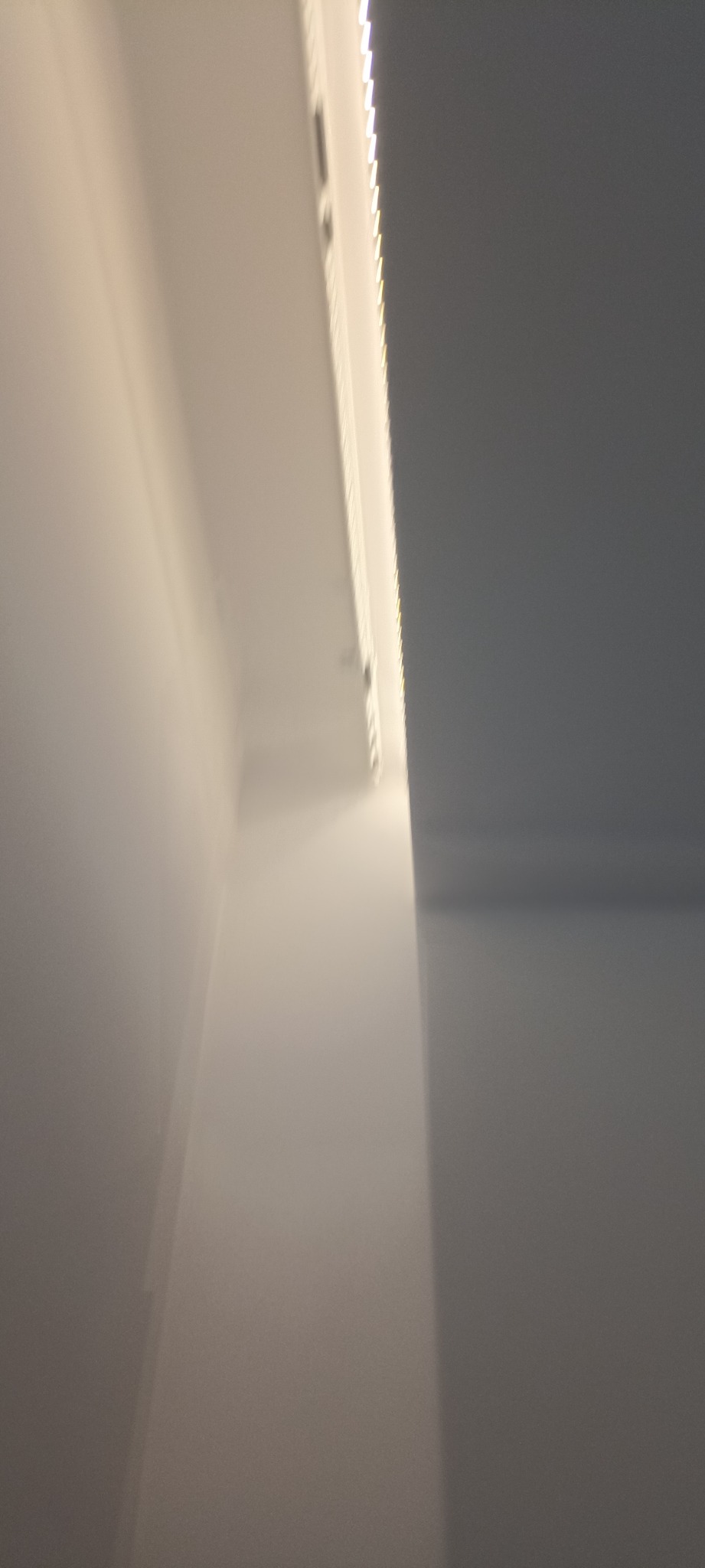 Biała ściana z zamontowanym oświetleniem LED wzdłuż sufitu, widok z dołu pod kątem, ukazujący minimalistyczny design i precyzję wykonania.