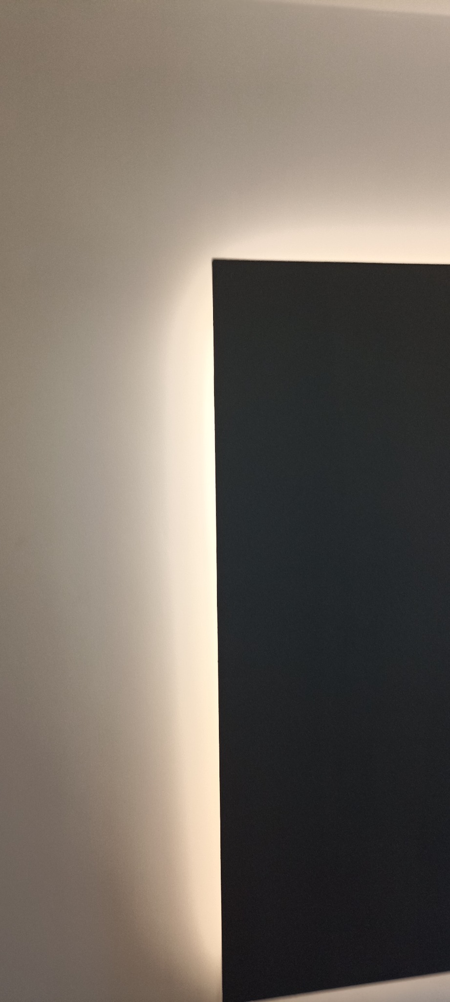 Fragment ściany po malowaniu na dwa kolory: jasny beż i grafit. Widoczne ostre przejście między kolorami i delikatne oświetlenie.