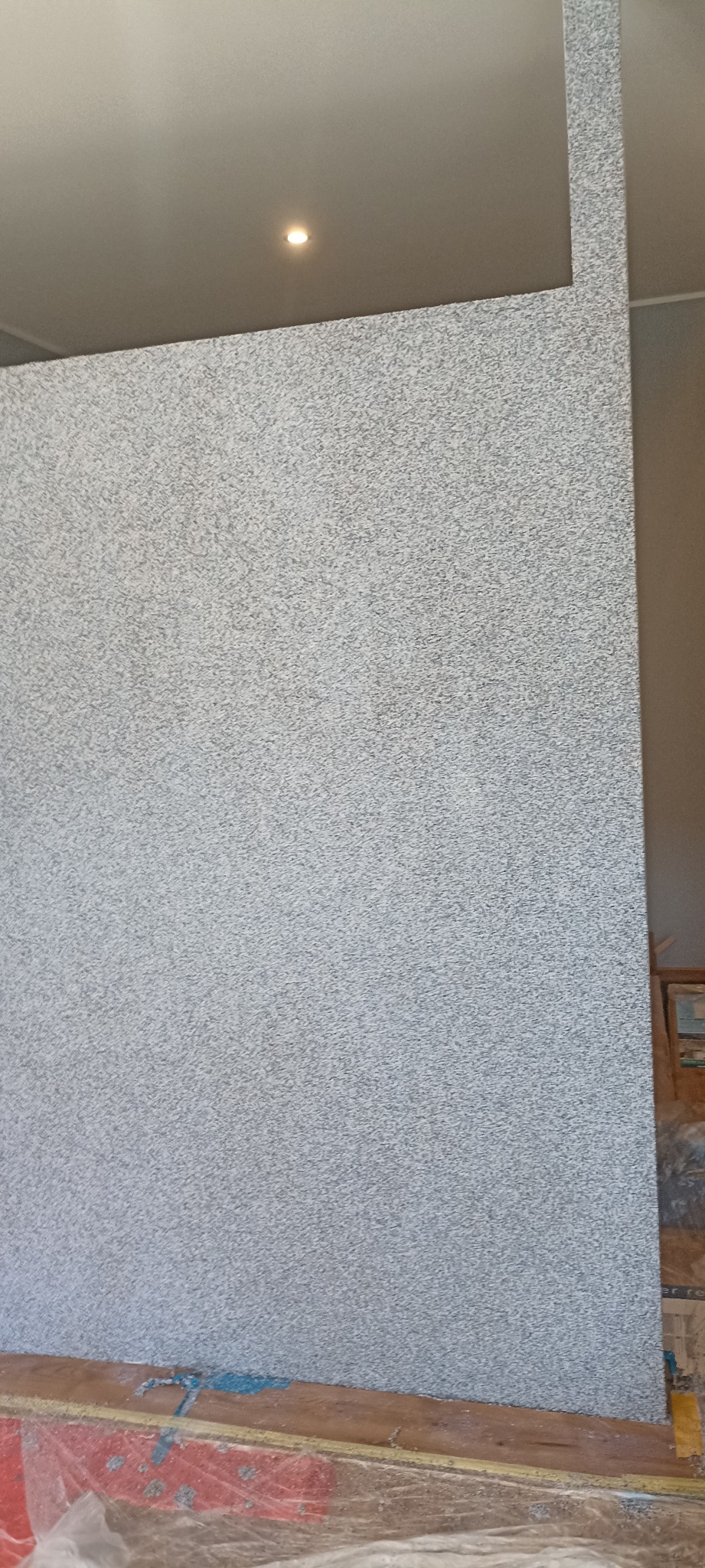 Ściana z dekoracyjną, szarą strukturą, widoczna dolna krawędź i fragment sufitu z oświetleniem punktowym. Wykończenie wnętrza w trakcie prac.