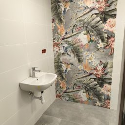 Ark - Biała umywalka z chromowaną baterią na tle ściany z białych płytek i dekoracyjnej mozaiki z motywem tropikalnych kwiatów i ptaków w wykończonej łazience.