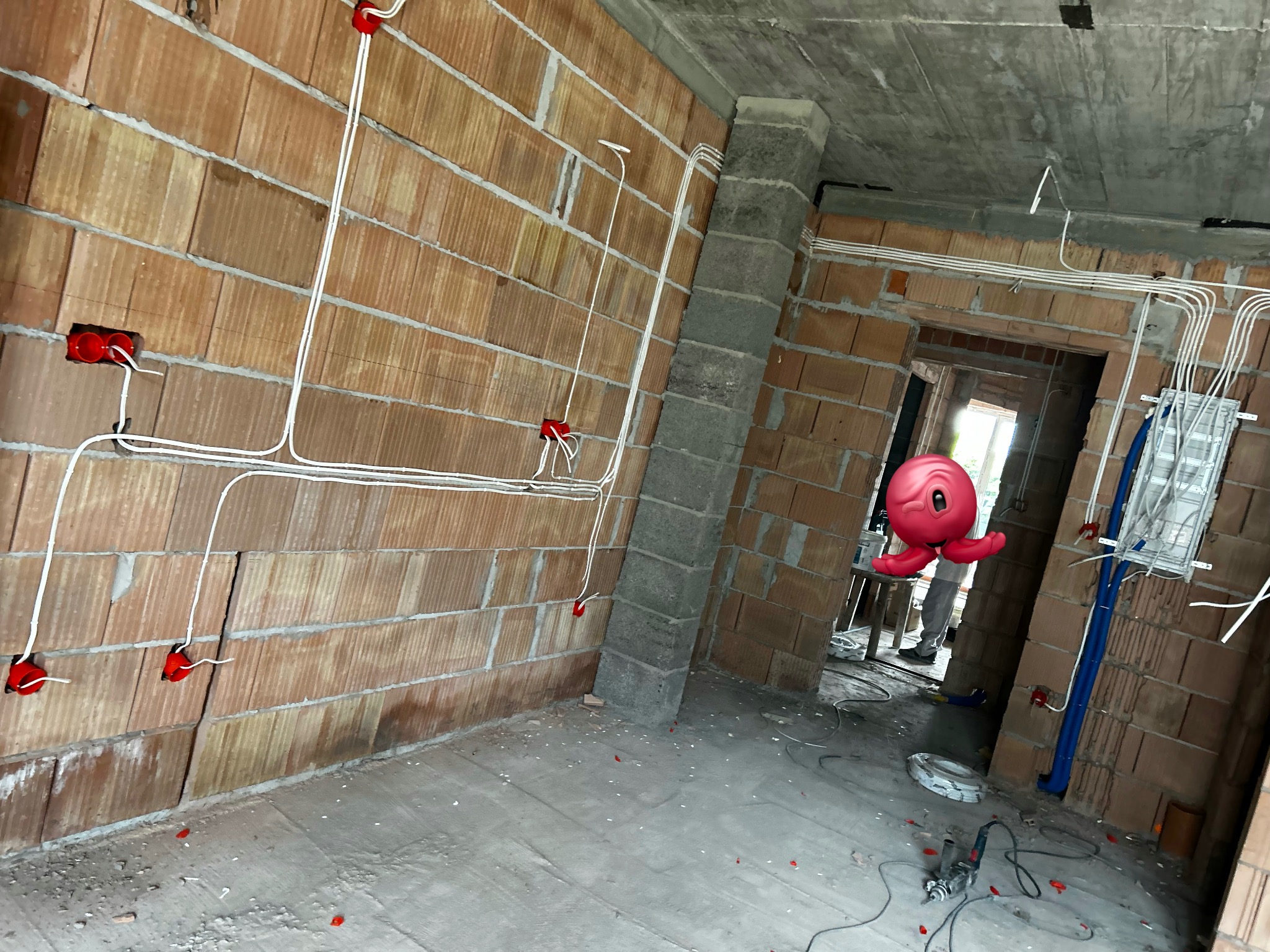 Surowy stan: instalacja elektryczna w budynku z czerwonej cegły. Widoczne kable w białych rurkach i czerwone puszki. Na podłodze narzędzia.