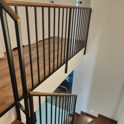 DAM-DAR METAL DAMIAN KRZEMIEŃ - Nowoczesne schody drewniane z czarną, metalową balustradą, widok z góry. Jasne wnętrze z drewnianą podłogą i schodami. Minimalistyczny design.