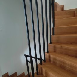 DAM-DAR METAL DAMIAN KRZEMIEŃ - Nowoczesne schody drewniane z czarną, minimalistyczną balustradą metalową. Jasne drewno stopni kontrastuje z ciemnym metalem. Ujęcie z dołu, podkreślające geometrię.