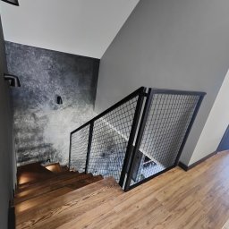 DAM-DAR METAL DAMIAN KRZEMIEŃ - Nowoczesne schody drewniane z czarną, metalową balustradą z siatki, oświetlone punktowo, na tle szarej ściany o fakturze betonu. Widok z góry.