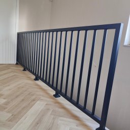 DAM-DAR METAL DAMIAN KRZEMIEŃ - Nowoczesna, czarna balustrada schodowa z pionowymi szczeblami, zamontowana na jasnej podłodze w jodełkę. Minimalistyczny design, widok z boku, neutralne tło.