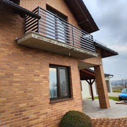 DAM-DAR METAL DAMIAN KRZEMIEŃ - Nowoczesna, pozioma balustrada balkonowa z czarnych profili na tle ceglanej elewacji domu. Widok z dołu, podkreślający minimalistyczny design i solidne wykonanie.