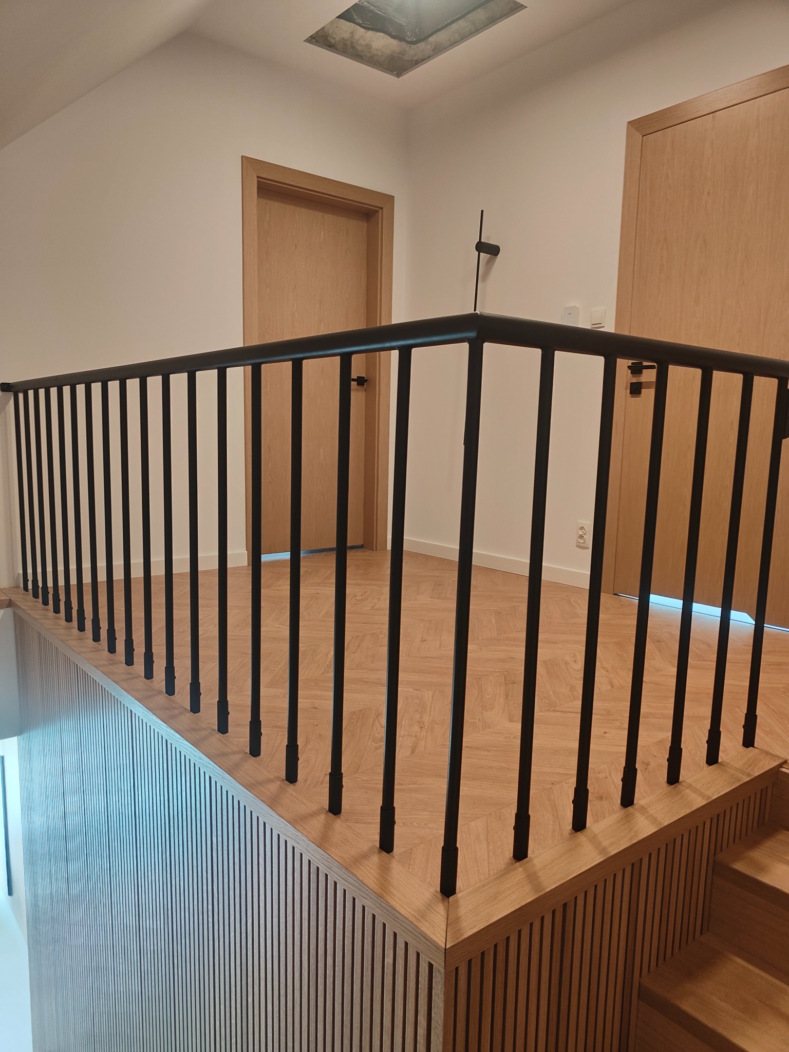 Czarna, metalowa balustrada na antresoli z drewnianym wykończeniem, widok z góry. Minimalistyczny design, jasne wnętrze z drewnianą podłogą i drzwiami.