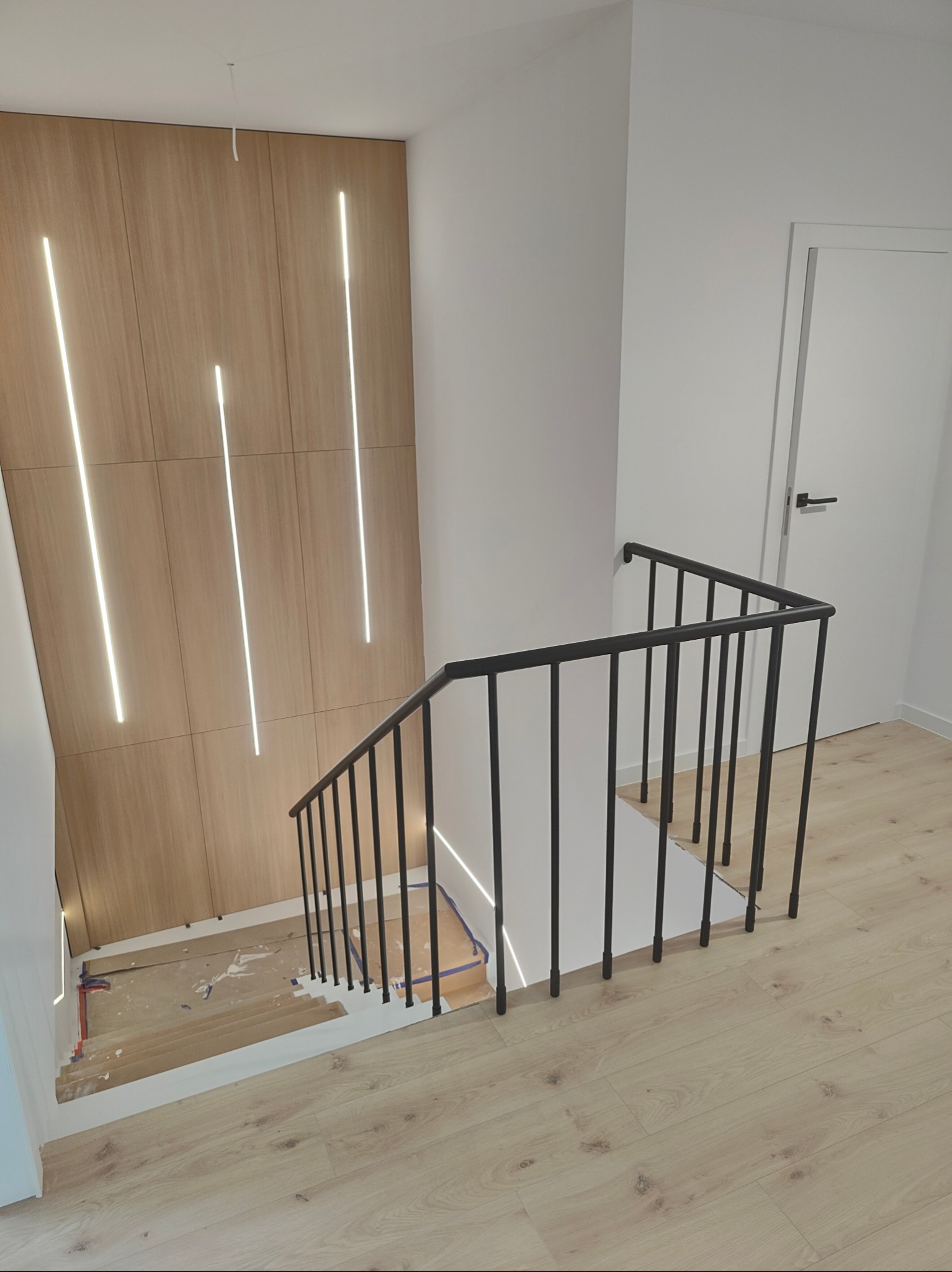 Nowoczesne schody z czarną balustradą i drewnianym wykończeniem ściany z oświetleniem LED. Widok z góry na dół, jasne wnętrze.