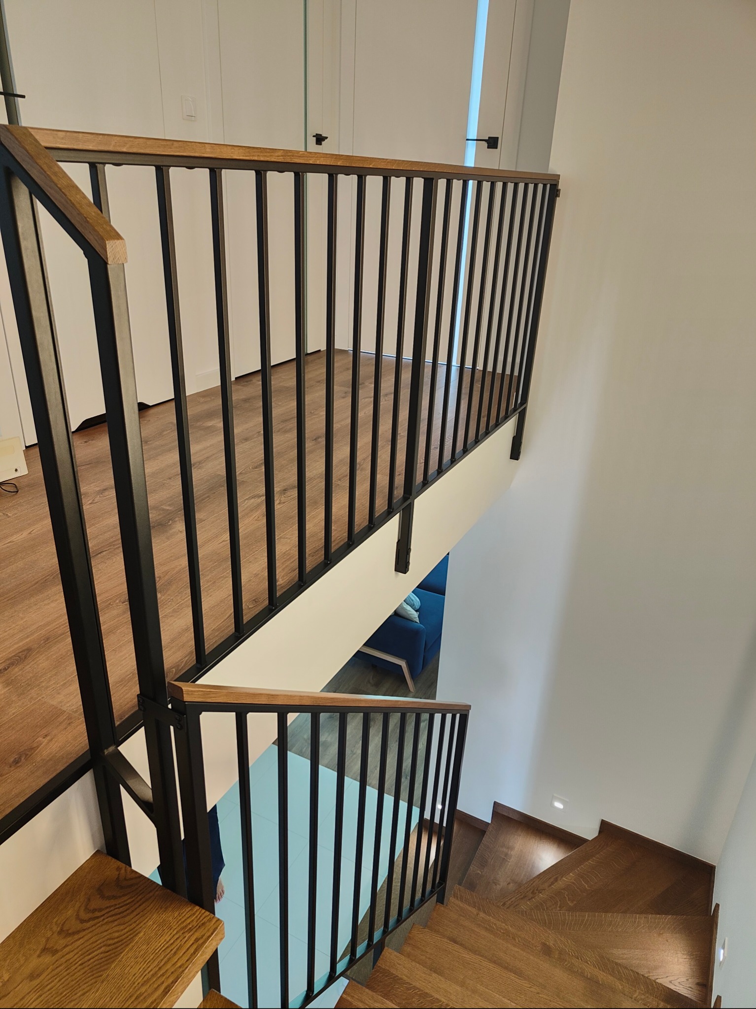 Nowoczesne schody drewniane z czarną, metalową balustradą, widok z góry. Jasne wnętrze z drewnianą podłogą i schodami. Minimalistyczny design.