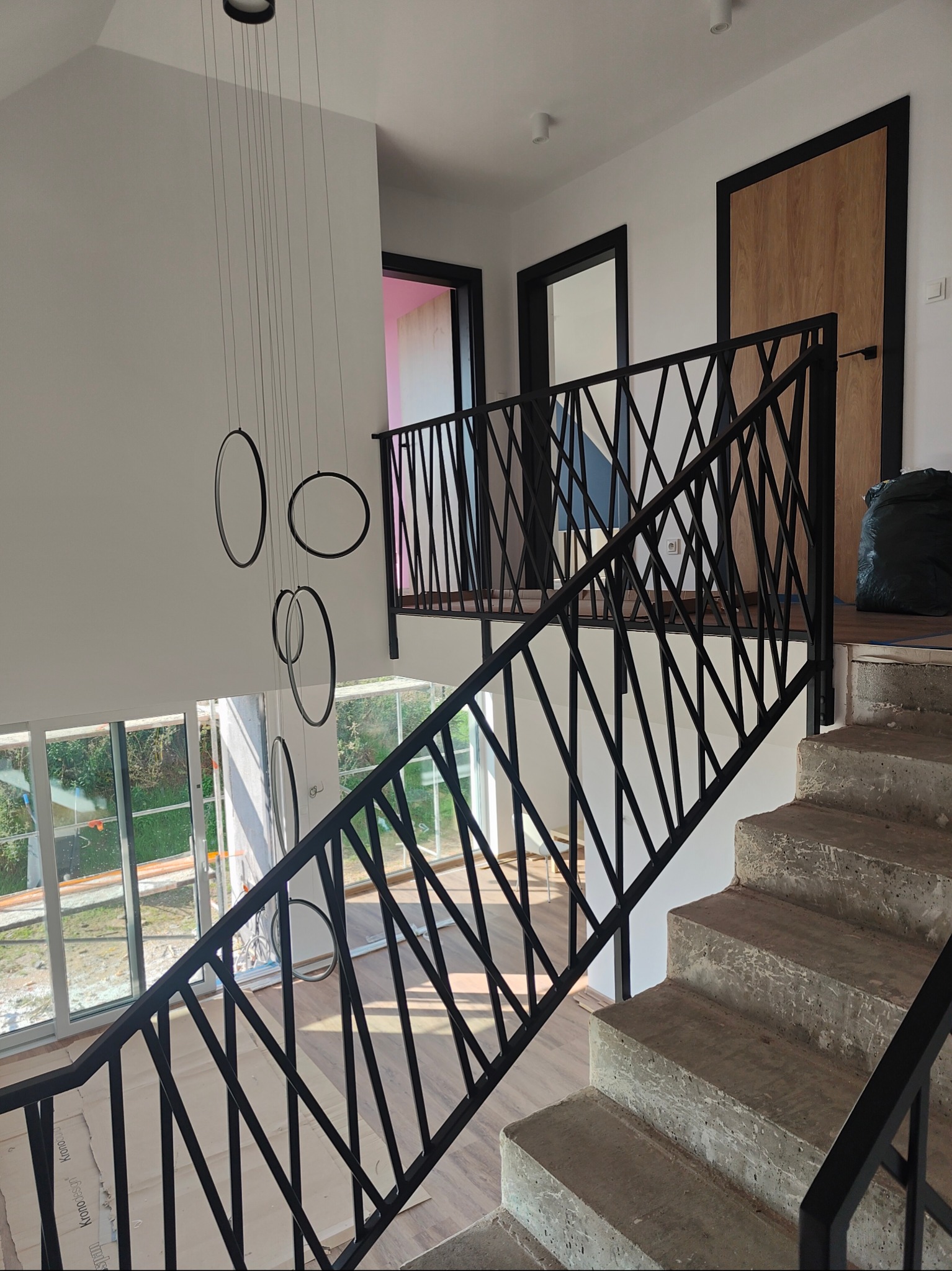 Nowoczesne schody betonowe z czarną, geometryczną balustradą metalową w jasnym wnętrzu domu. Widok z góry, wiszące lampy w kształcie okręgów.