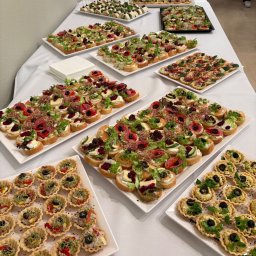 Eco Store - Stół cateringowy z różnorodnymi przekąskami: tartaletki z pastą, kanapki z warzywami i wędlinami, ułożone na białych talerzach. Widoczne białe serwetki i talerze.