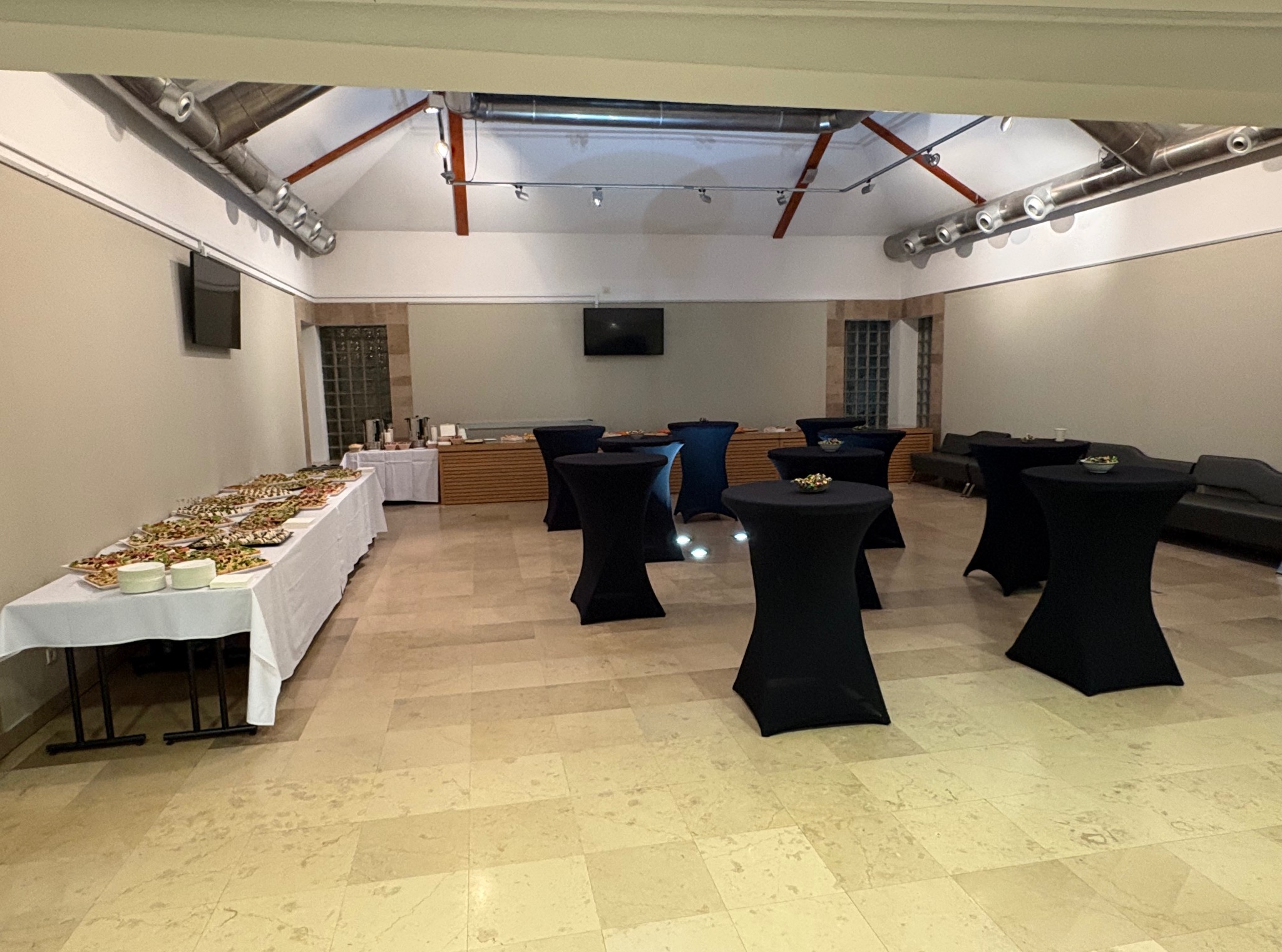 Elegancka sala bankietowa w Warszawie z bufetem i stolikami koktajlowymi, gotowa na przyjęcie. Oświetlenie sufitowe i jasna podłoga.