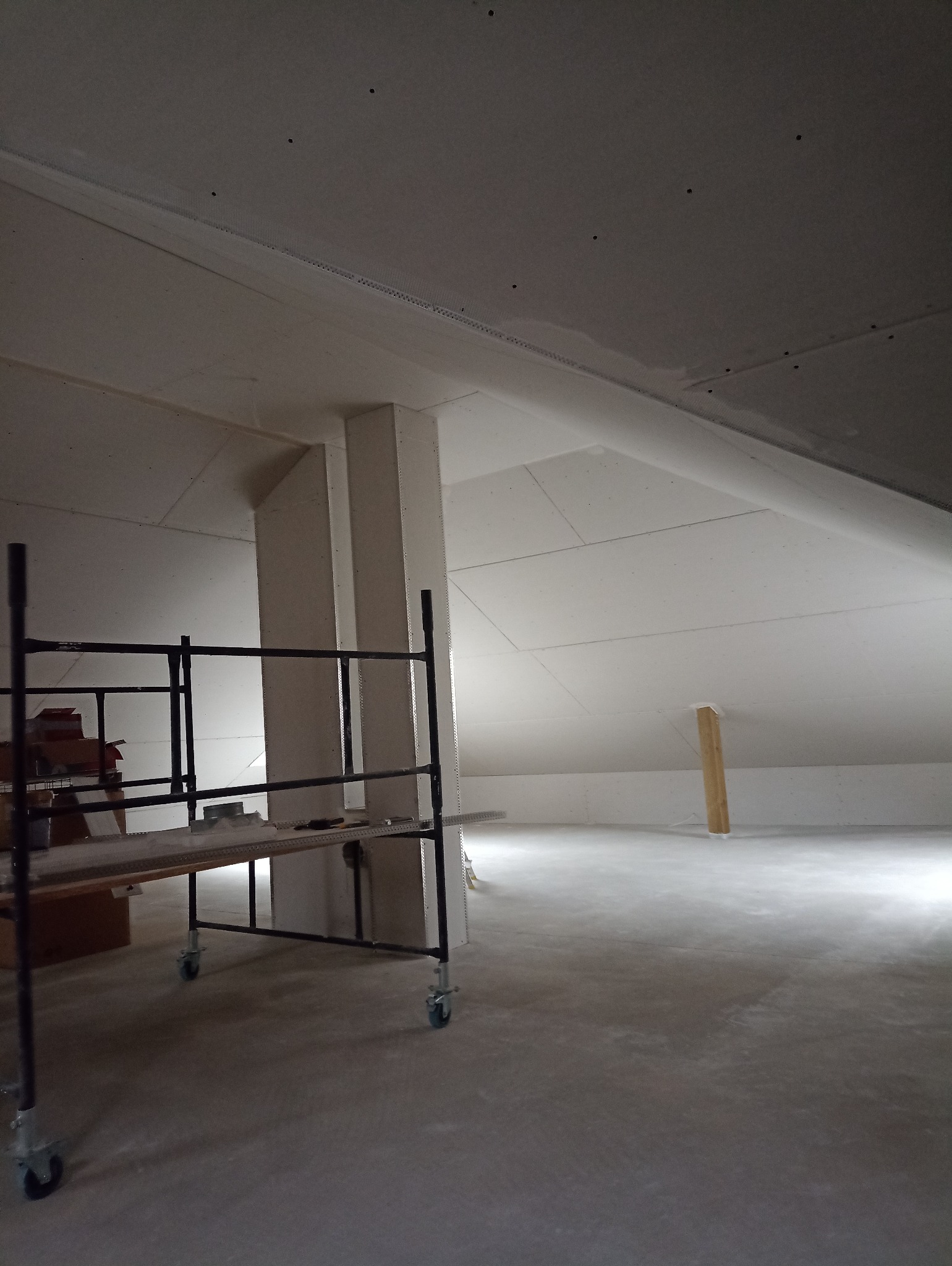 Poddasze z zamontowaną płytą karton-gips na skosach i suficie, widoczne rusztowanie na kółkach, przygotowane do dalszych prac wykończeniowych.