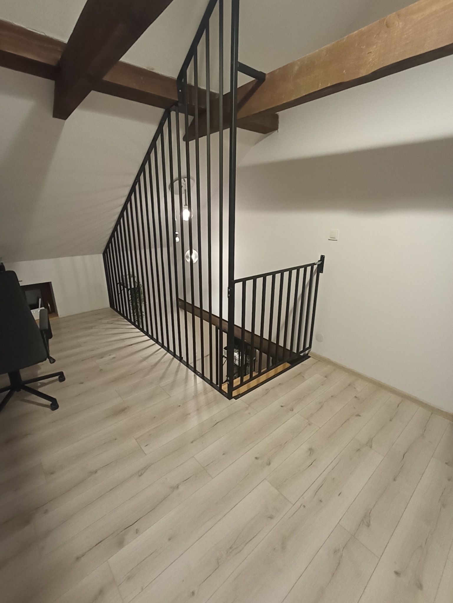 Nowoczesna, czarna balustrada metalowa na antresoli w Żurawcu, z drewnianymi belkami stropowymi w tle. Minimalistyczny design, jasna podłoga, widok z dołu.
