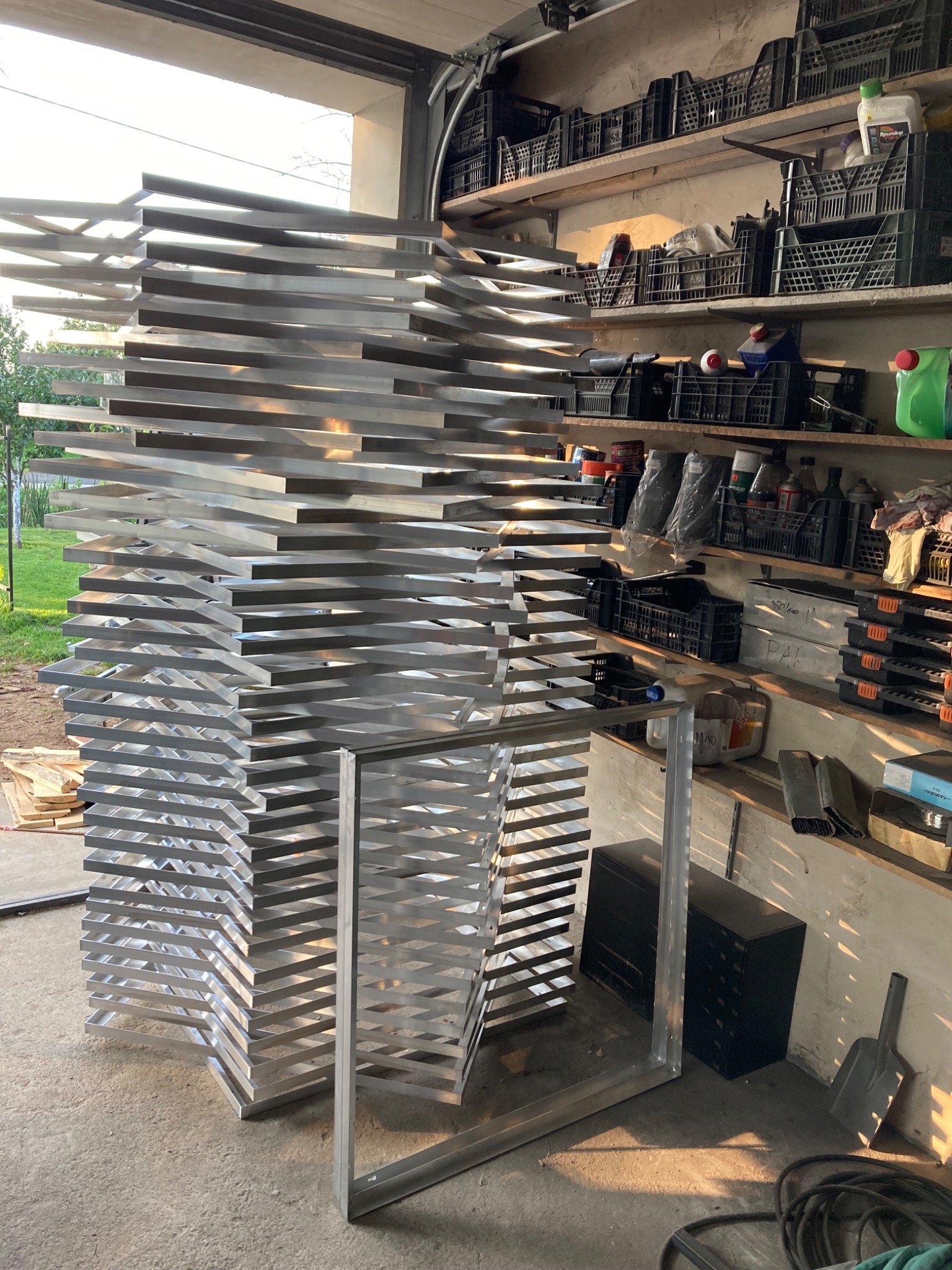 Stos metalowych, aluminiowych profili w warsztacie, przygotowanych do konstrukcji balustrady lub ogrodzenia. Widoczne narzędzia i regały z akcesoriami.