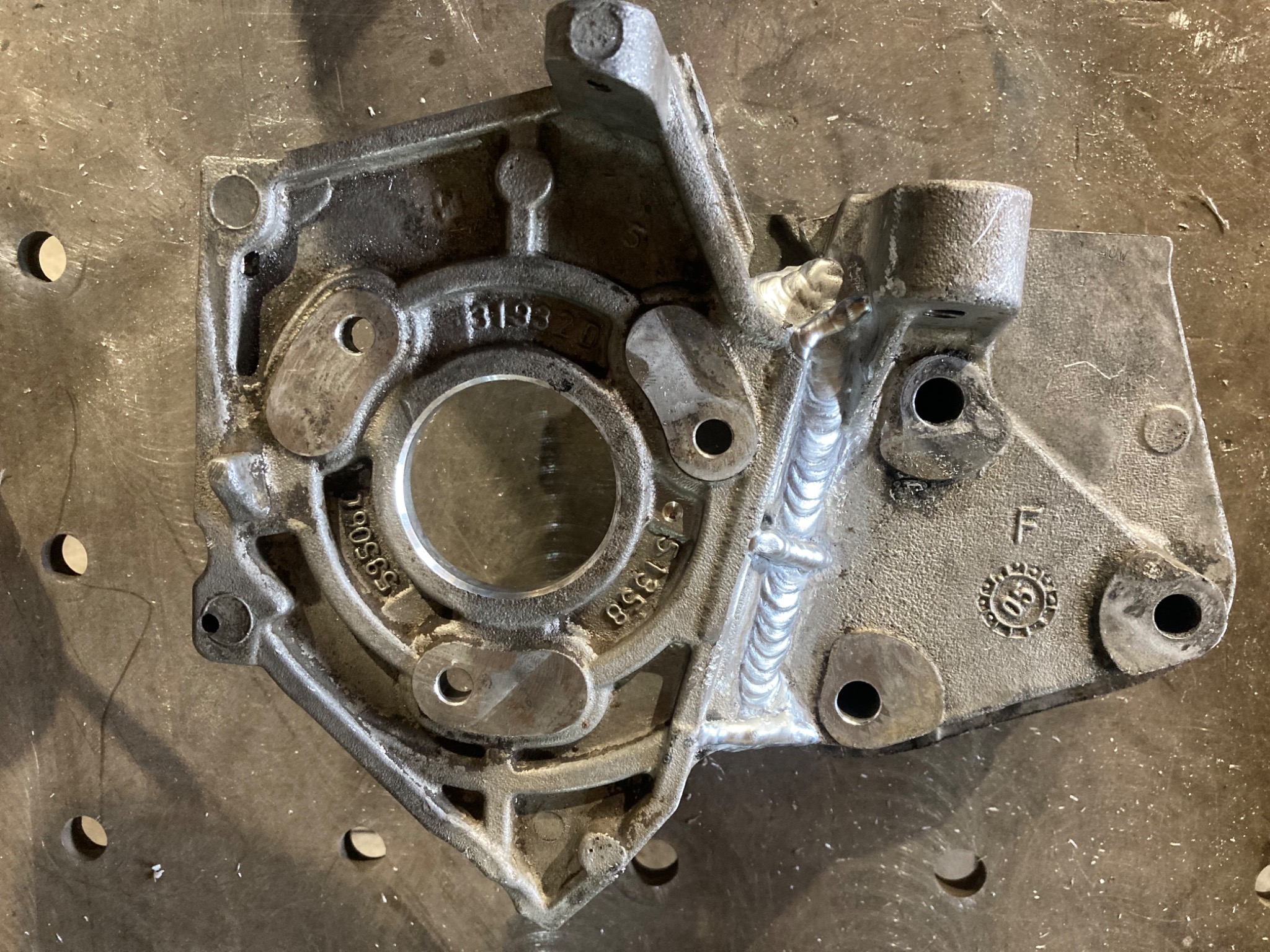 Szczegół metalowej konstrukcji po spawaniu, widoczne ślady obróbki i numery seryjne. Metalowa powierzchnia z otworami i śladami spawania.