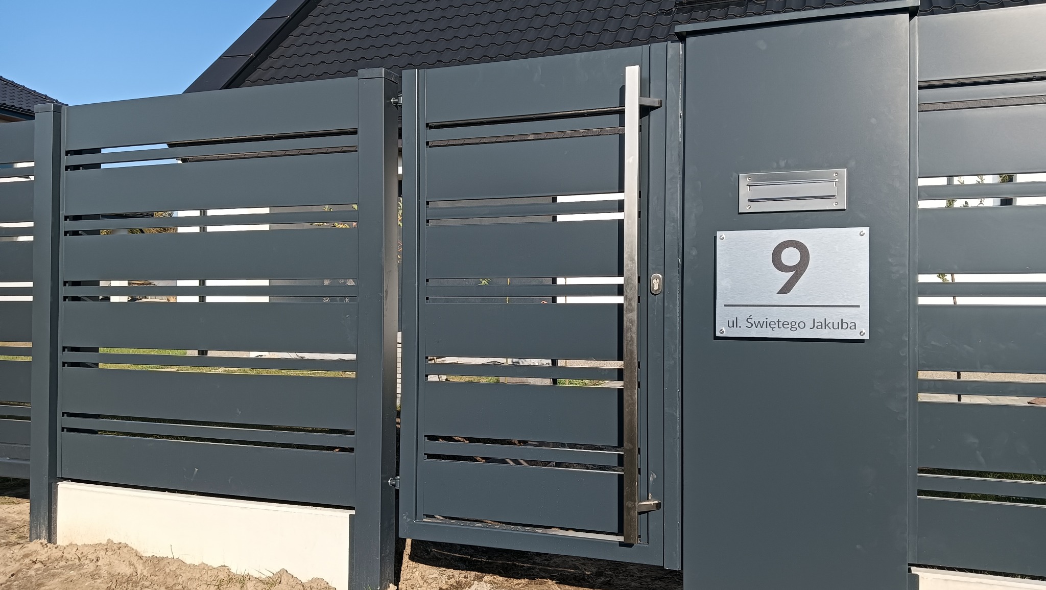 Nowoczesna, grafitowa brama wjazdowa z poziomymi szczeblami i numerem domu '9 ul. Świętego Jakuba', zintegrowana ze skrzynką na listy.