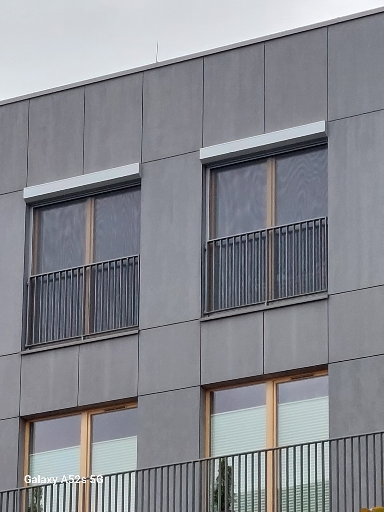 Elewacja budynku z dwoma oknami zabezpieczonymi moskitierami i zwiniętymi roletami zewnętrznymi w szarych kasetach. Na dole widoczne plisy w oknach.