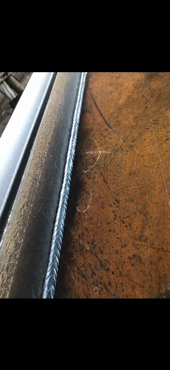 Spoina łącząca dwa elementy metalowe, widoczna z bliska, z charakterystycznym wzorem i lekkim połyskiem, na tle powierzchni z rdzawym nalotem.