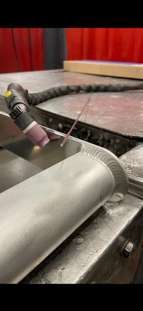 Precyzyjne łączenie metalowych elementów metodą TIG, widoczne spawy o regularnym wzorze na krawędziach. Detal pracy z bliska, narzędzie w kadrze.