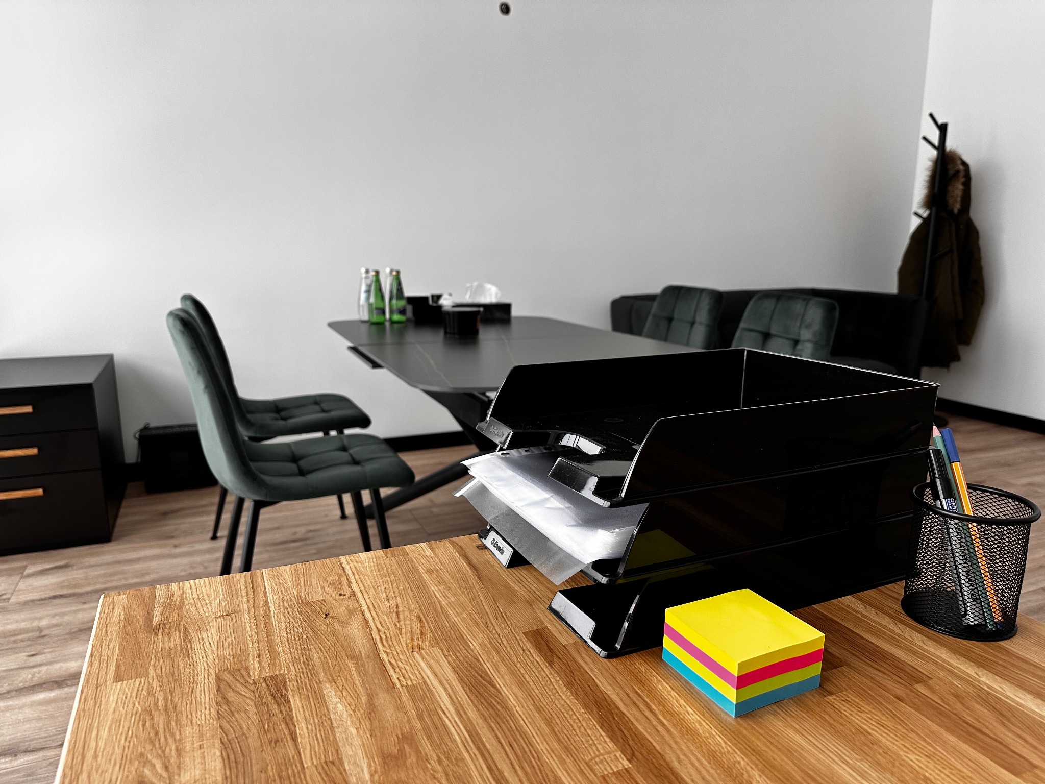 Nowoczesne biuro adwokackie: czarny stół konferencyjny, zielone krzesła, drewniane biurko z organizerem na dokumenty i kolorowymi karteczkami samoprzylepnymi.