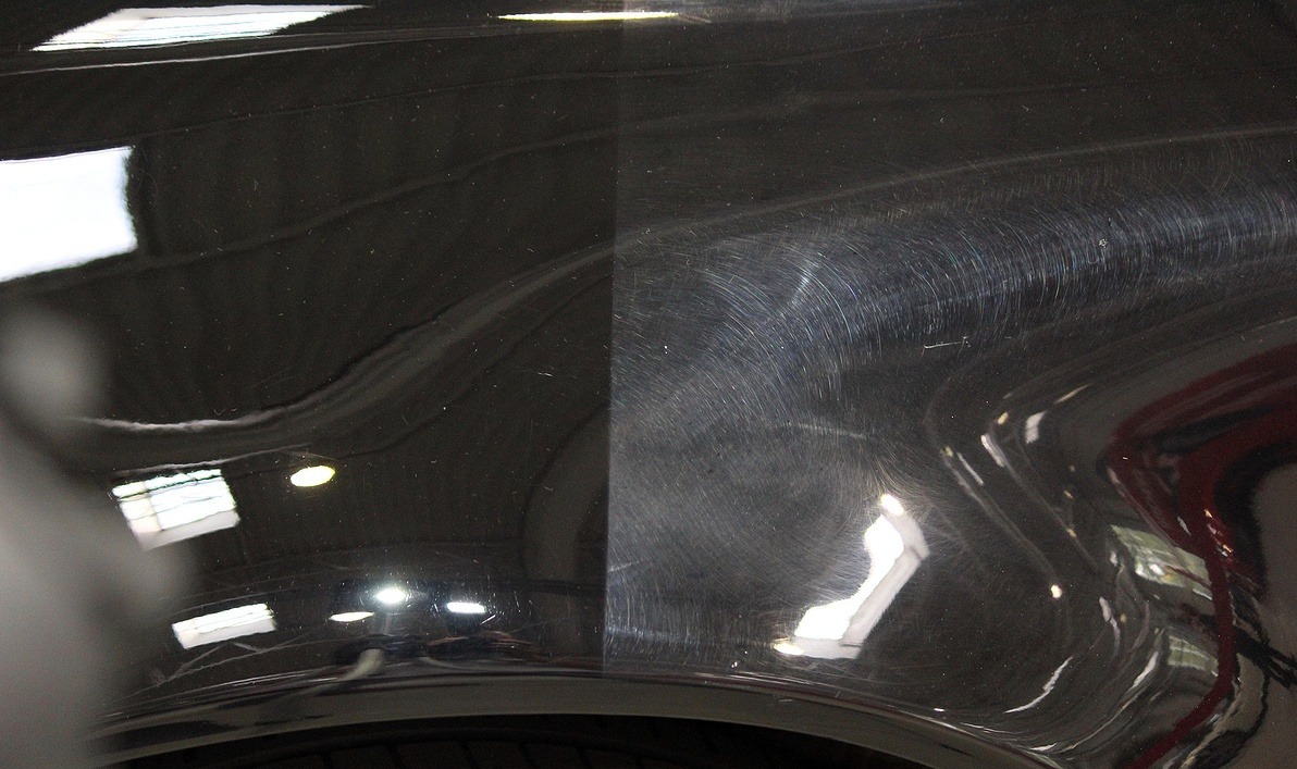 Część karoserii czarnego auta, po lewej wypolerowana, po prawej zarysowania. Efekt polerowania lakieru samochodowego, widoczne odbicie światła.