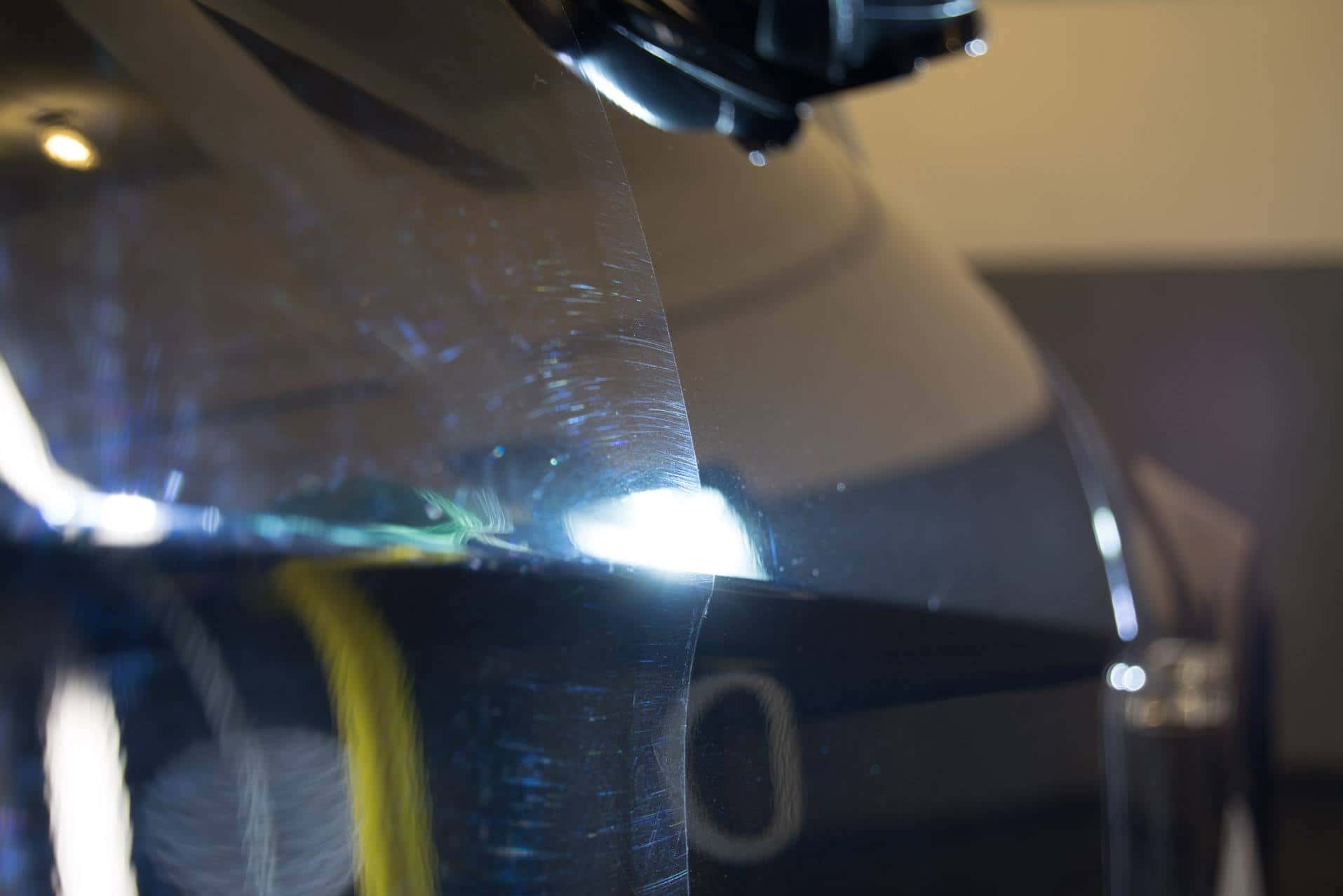 Błyszczący, ciemny lakier samochodowy z widocznymi rysami pod intensywnym światłem lampy inspekcyjnej, ukazujący stan przed polerowaniem.