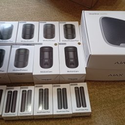 GUARDSD Serhii Drynkov - Zestaw komponentów systemu alarmowego Ajax w oryginalnych opakowaniach: czujniki ruchu, otwarcia drzwi i syrena alarmowa. Widoczne modele MotionProtect, DoorProtect i StreetSiren.