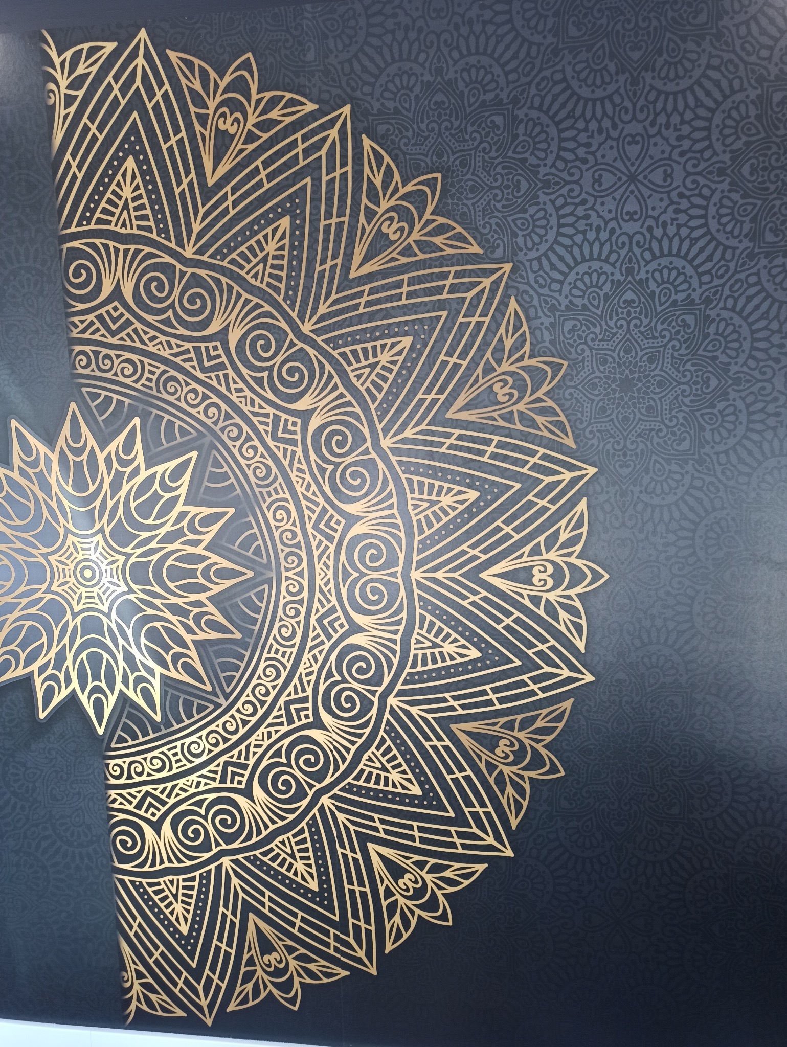 Dekoracyjna ściana w odcieniach szarości z elementami złotej mandali. Geometryczny wzór na ścianie, widoczny fragment dekoracji.