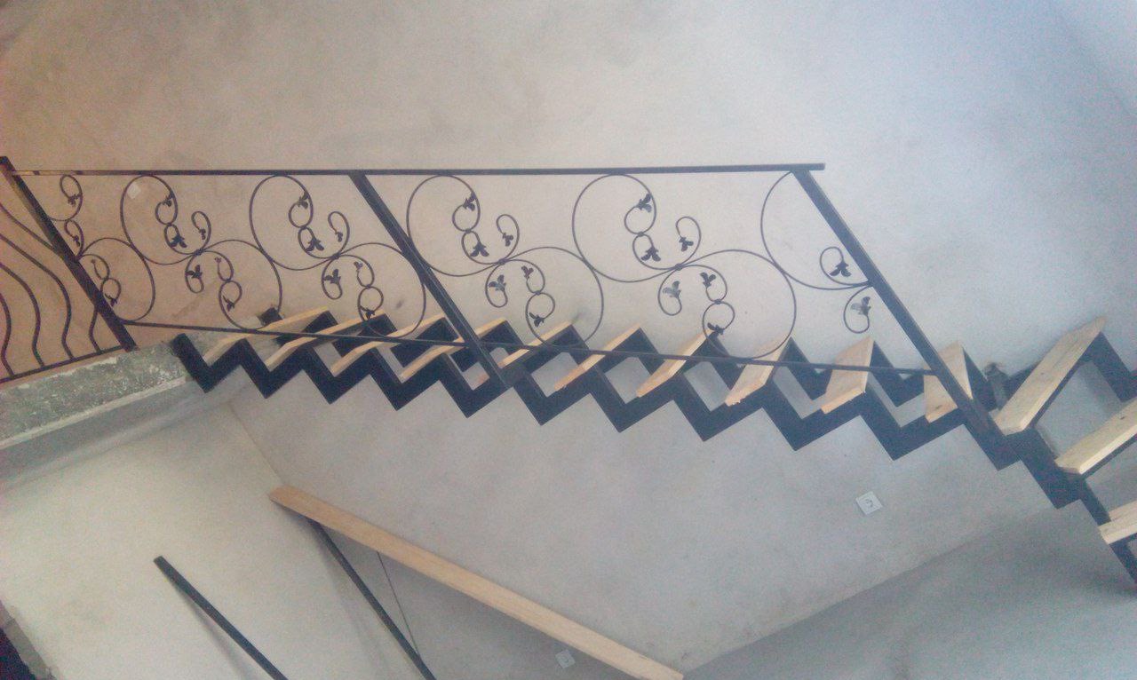 Metalowe schody z ozdobną, kutą balustradą w stylu retro. Widok z góry ukazuje zygzakowaty kształt stopni i delikatne zdobienia poręczy.