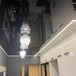 Firma Remontowo Budowlana LOFTIS Sebastian Jakubowski - Błyszczący, czarny sufit z trzema kryształowymi żyrandolami. Białe szafy z oświetleniem LED i drewniane drzwi tworzą eleganckie wykończenie wnętrza.