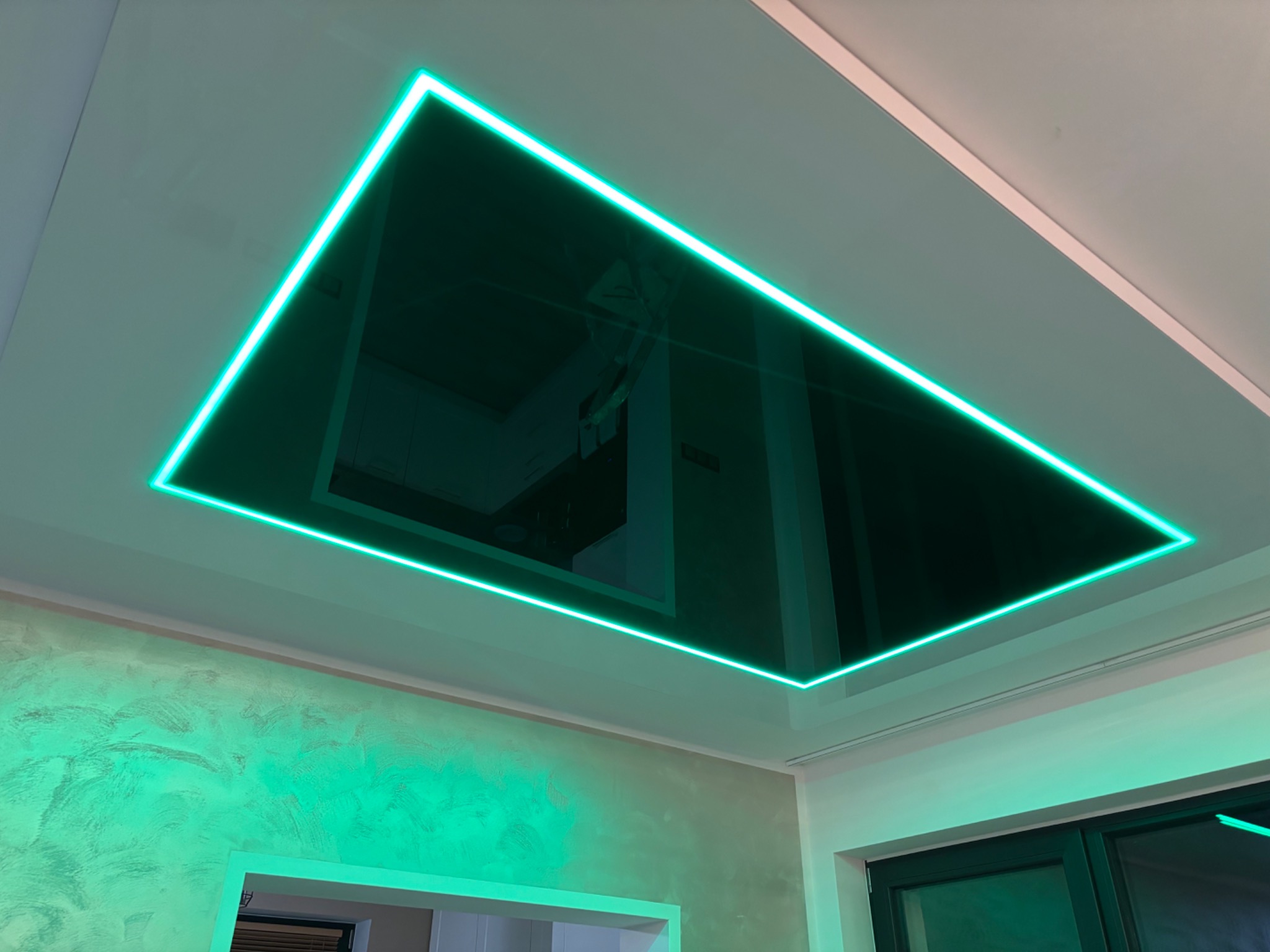 Nowoczesny sufit z podświetleniem LED w kształcie prostokąta, odbijający wnętrze pomieszczenia. Ściana z dekoracyjną fakturą w odcieniach zieleni.