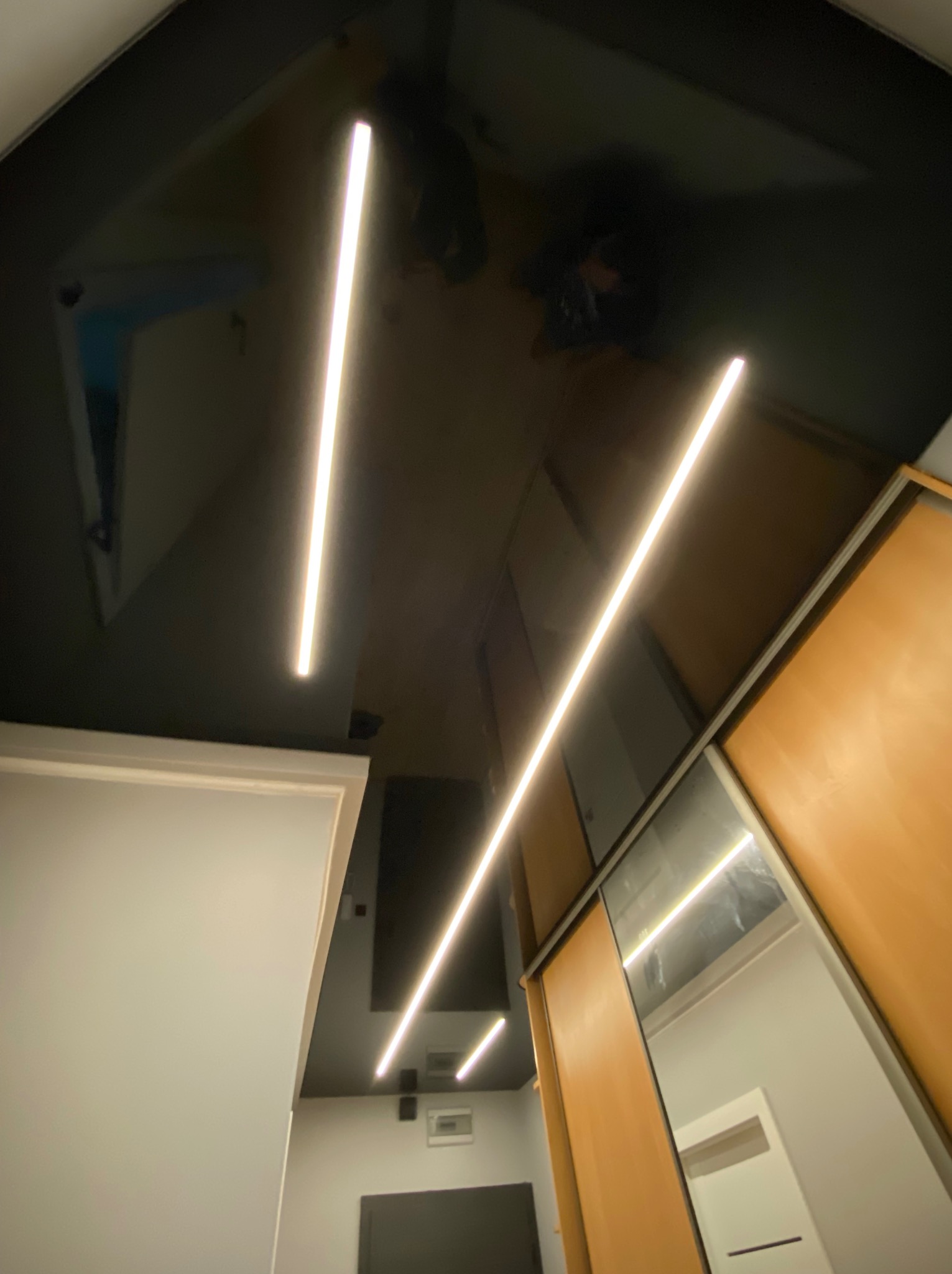 Błyszczący, czarny sufit napinany z liniowym oświetleniem LED w Oleśnicy Małej. Widoczne odbicie wnętrza i fragment szafy w zabudowie.