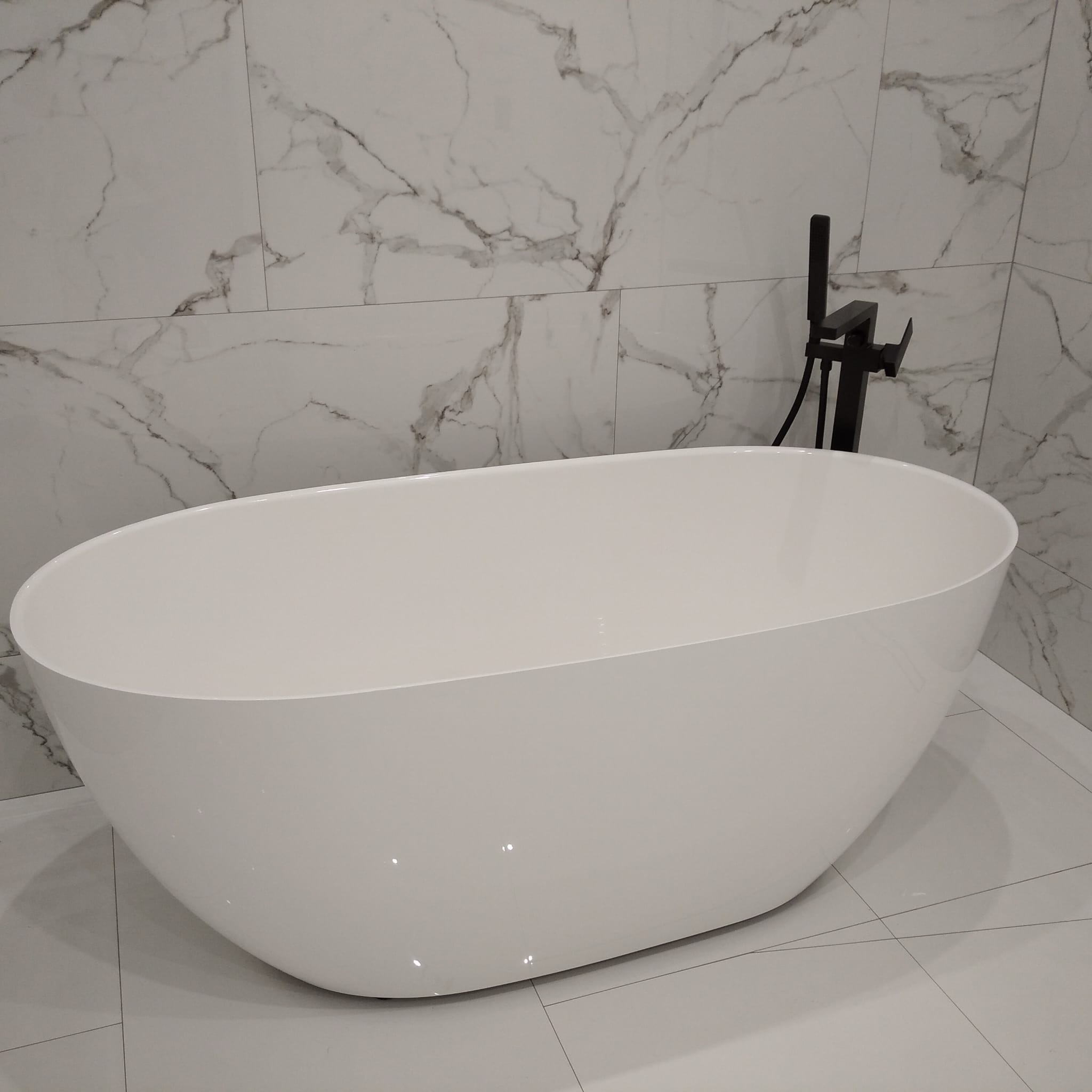 Biała, wolnostojąca wanna owalna z czarną armaturą na tle marmurowych płytek w łazience. Minimalistyczny design, nowoczesne wykończenie.