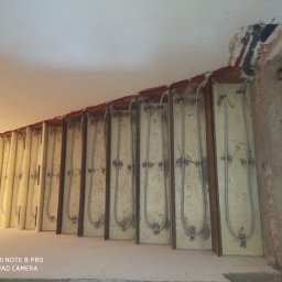 Wojciech woj - Montaż ogrzewania podłogowego w izolowanych panelach, widoczne rury grzewcze przed wylewką. Fragment instalacji przy suficie z widocznymi przewodami.