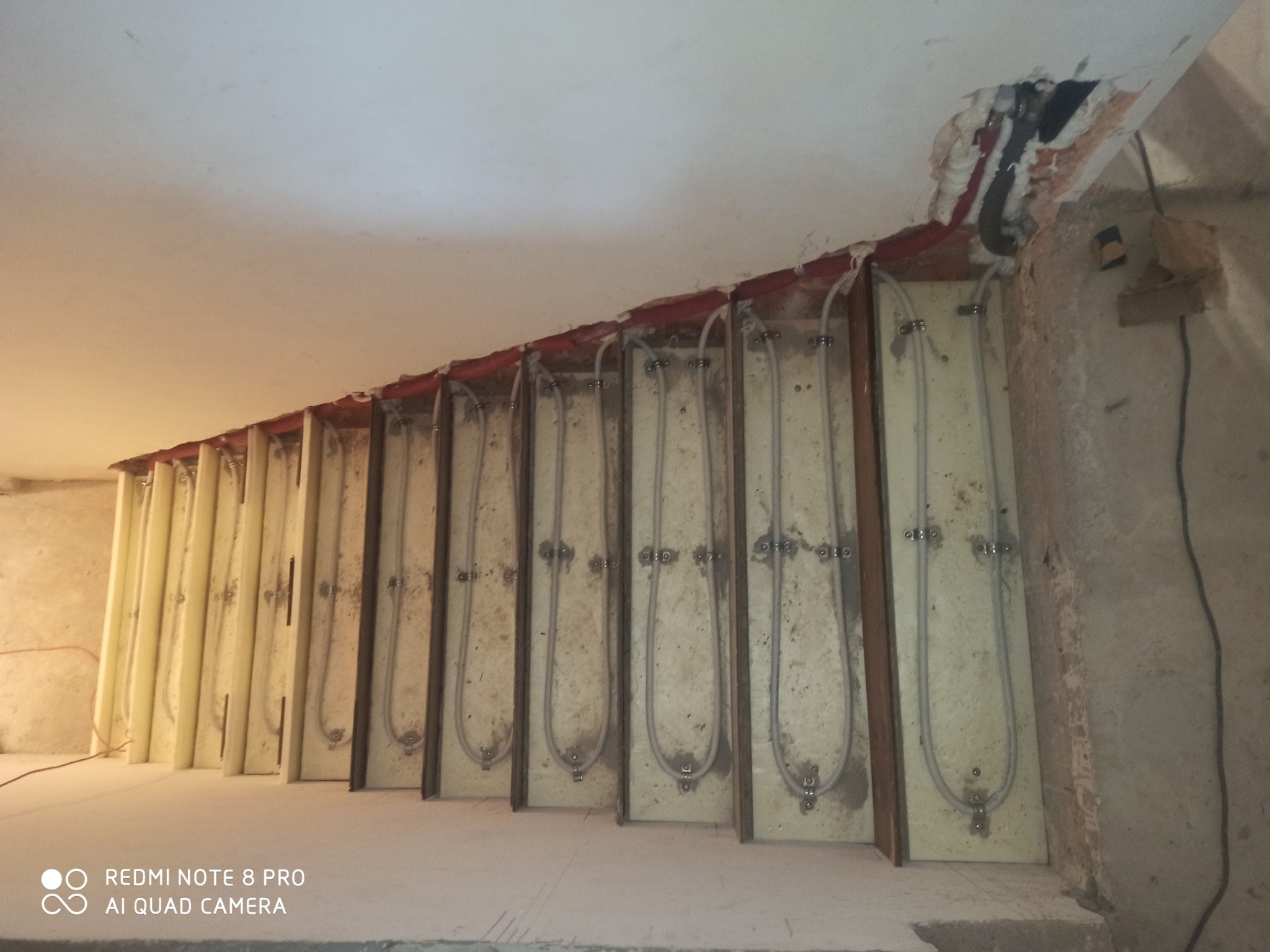 Montaż ogrzewania podłogowego w izolowanych panelach, widoczne rury grzewcze przed wylewką. Fragment instalacji przy suficie z widocznymi przewodami.