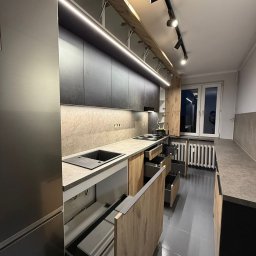 Piotr Warulik - Nowoczesna kuchnia z szarymi frontami i drewnianymi akcentami, oświetlenie LED podszafkowe, otwarte szuflady cargo. Realizacja w Tychach.